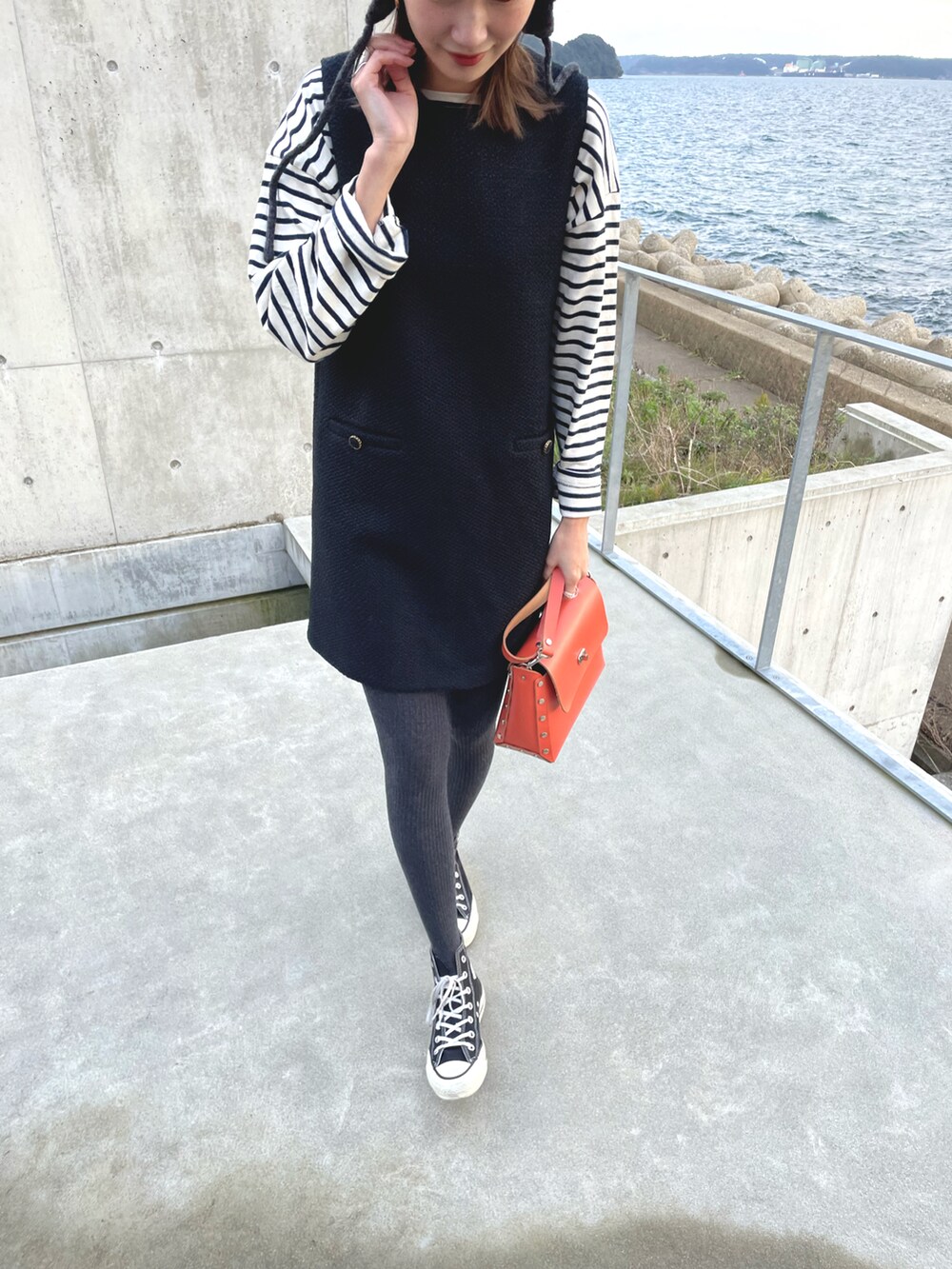 オレンジ系のバッグ、ブラック系のワンピース/ドレス、ブラック系のスニーカーを着用したレディースの冬コーディネートの2枚目の写真