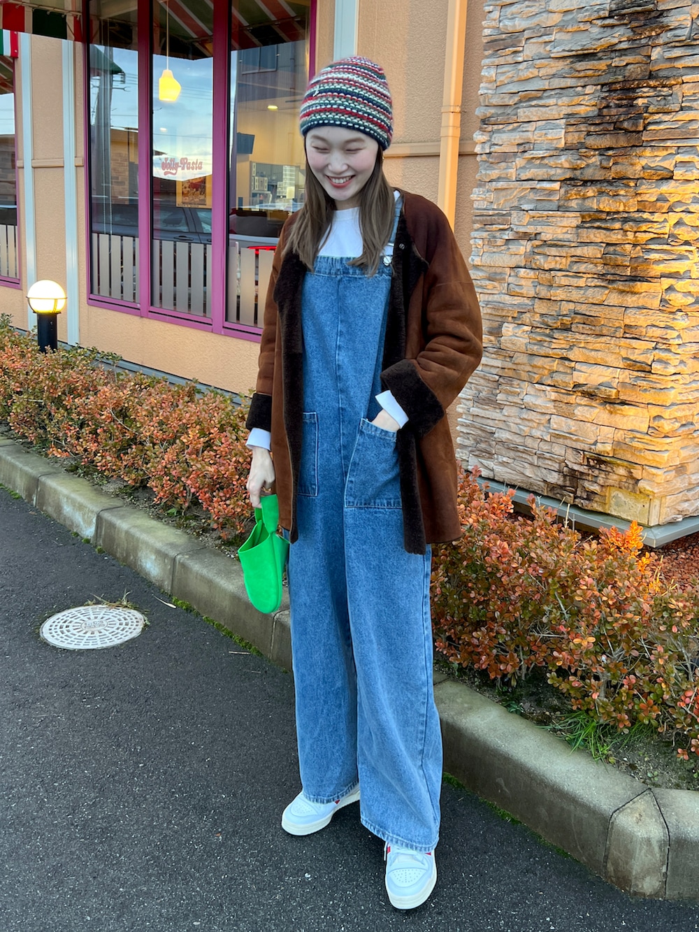 ブルー系のサロペット/オーバーオール、ホワイト系のスニーカー、ブラウン系のムートンコートを着用したレディースの冬コーディネートの2枚目の写真