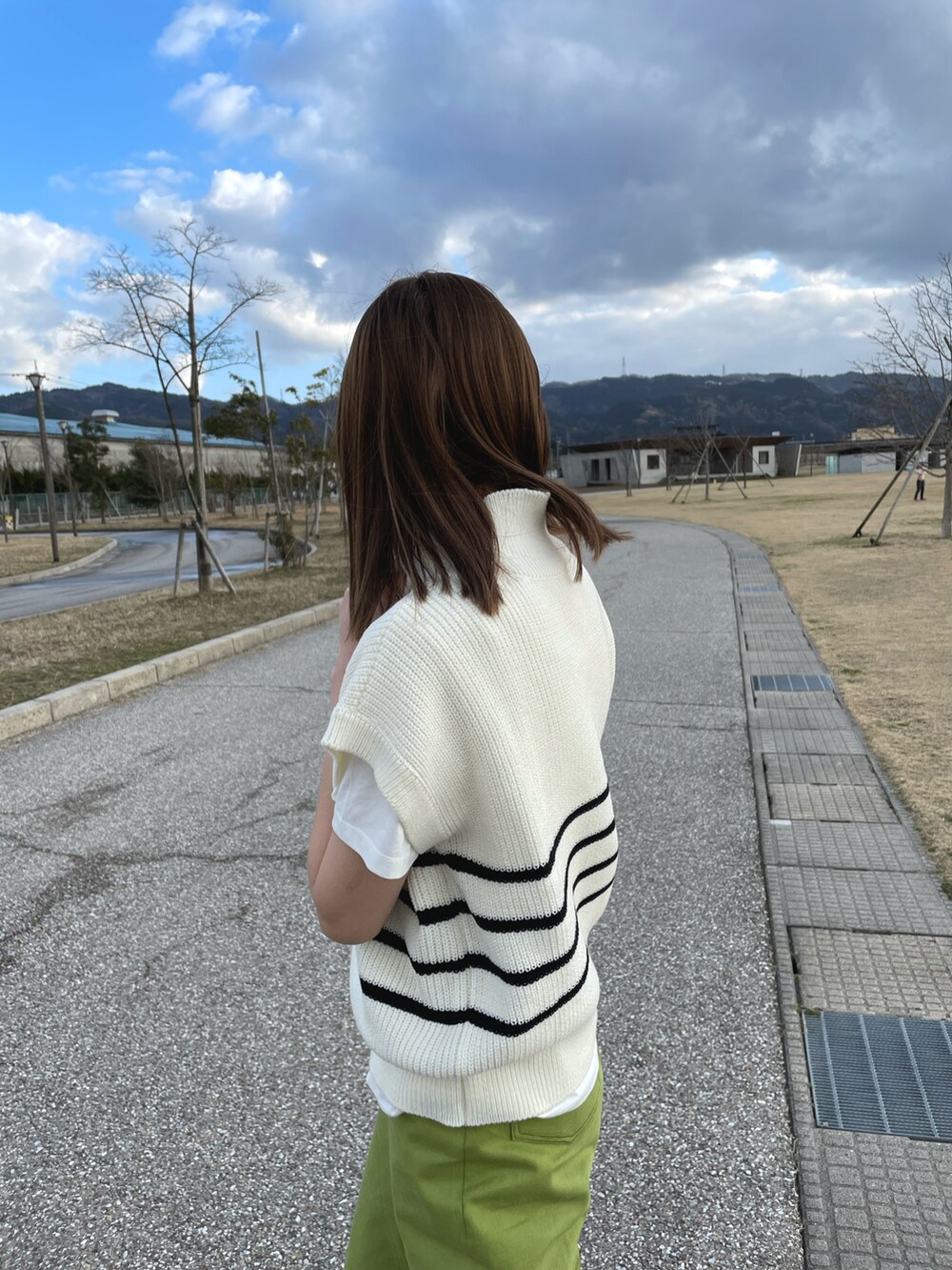 ホワイト系のベスト、グリーン系のパンツ、ブラック系のスニーカーを着用したレディースの春コーディネートの2枚目の写真