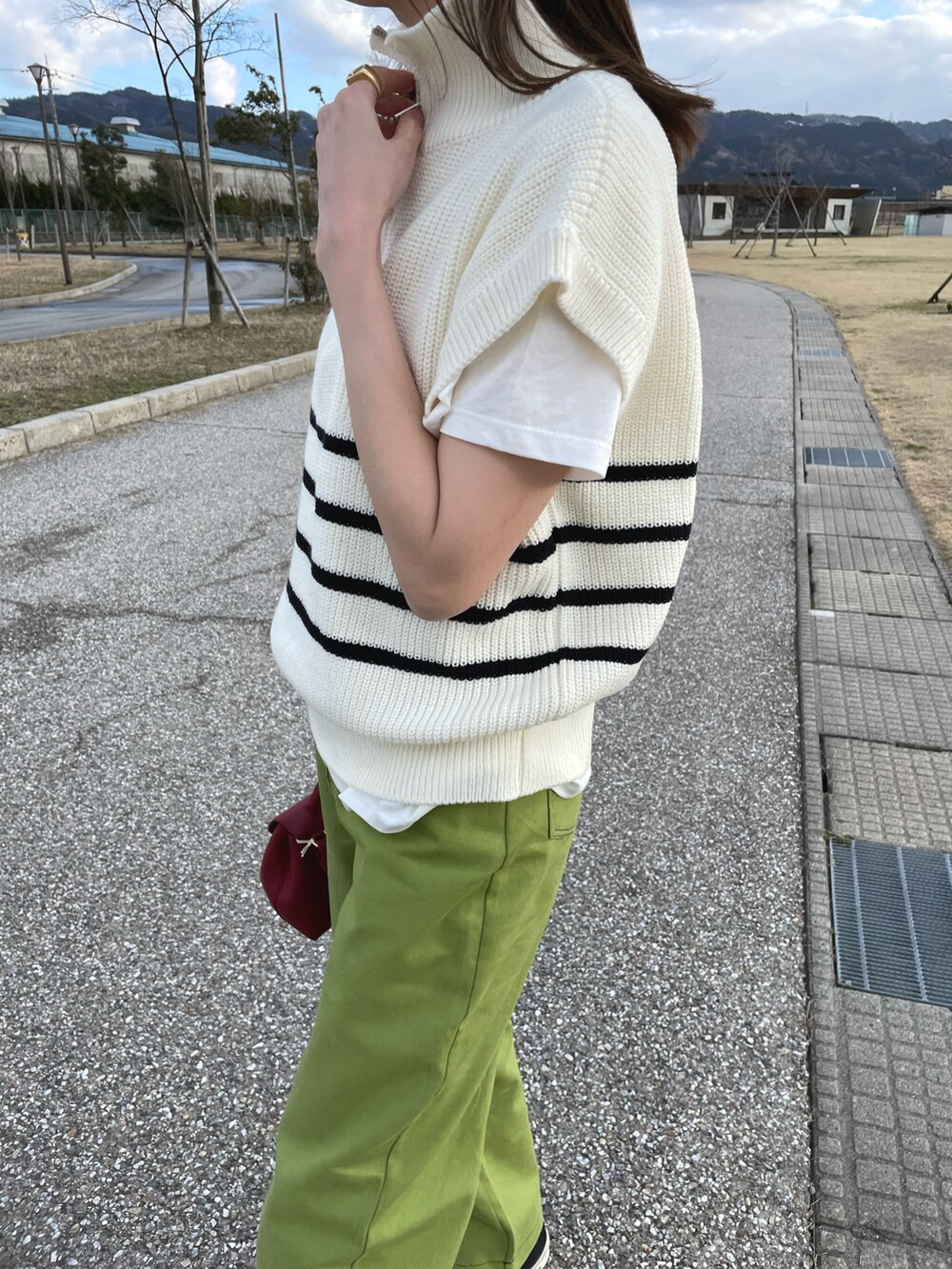 ホワイト系のベスト、グリーン系のパンツ、ブラック系のスニーカーを着用したレディースの春コーディネートの3枚目の写真