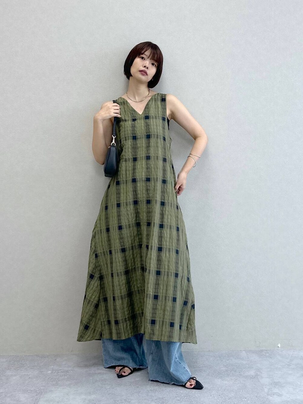 ブルー系のデニムパンツ、グリーン系のワンピース、ブラック系のショルダーバッグを着用したレディースの夏コーディネートの2枚目の写真