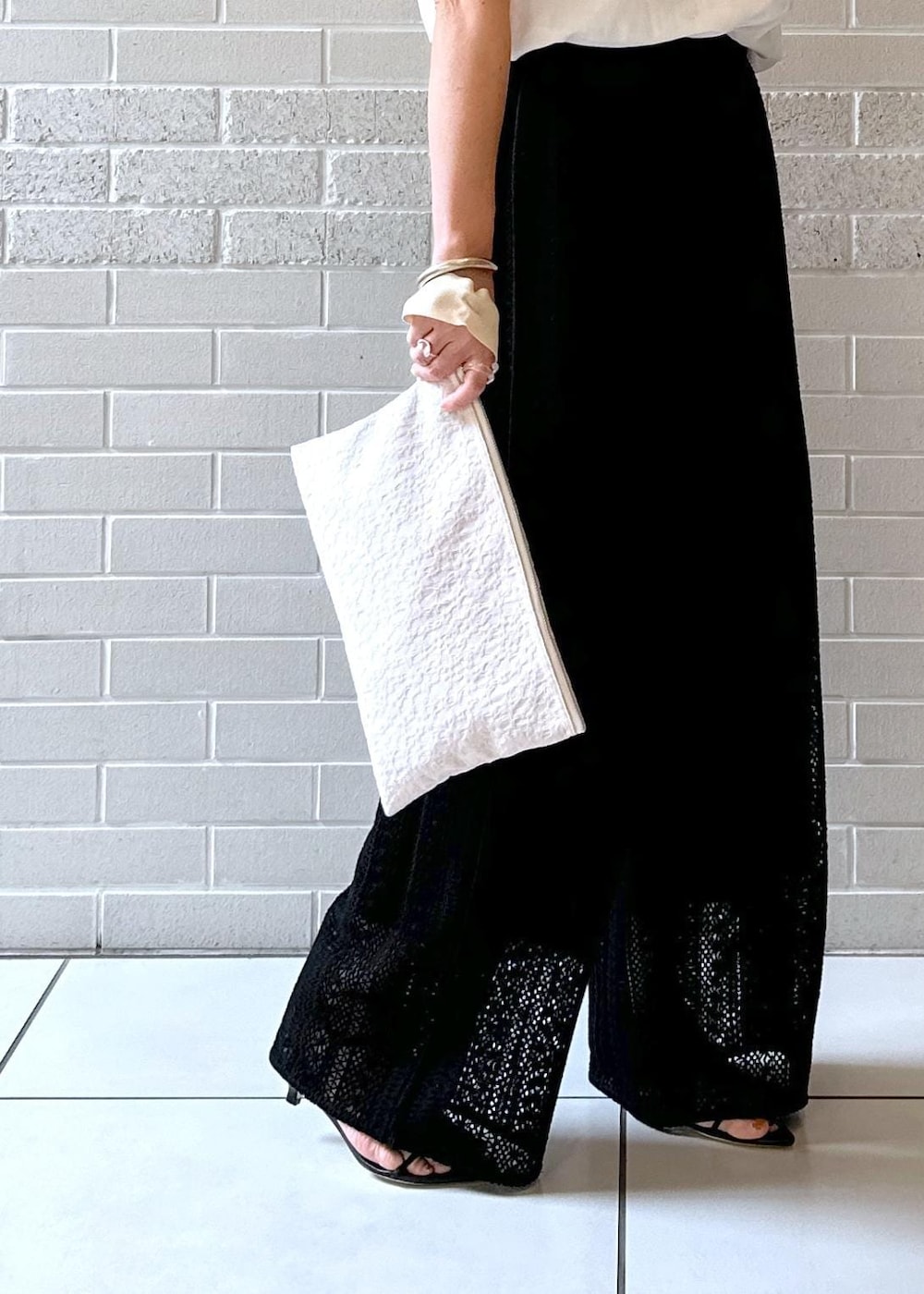 ブラック系のその他パンツ、ブラック系のサンダル、ベージュ系のクラッチバッグを着用したレディースの夏コーディネートの6枚目の写真