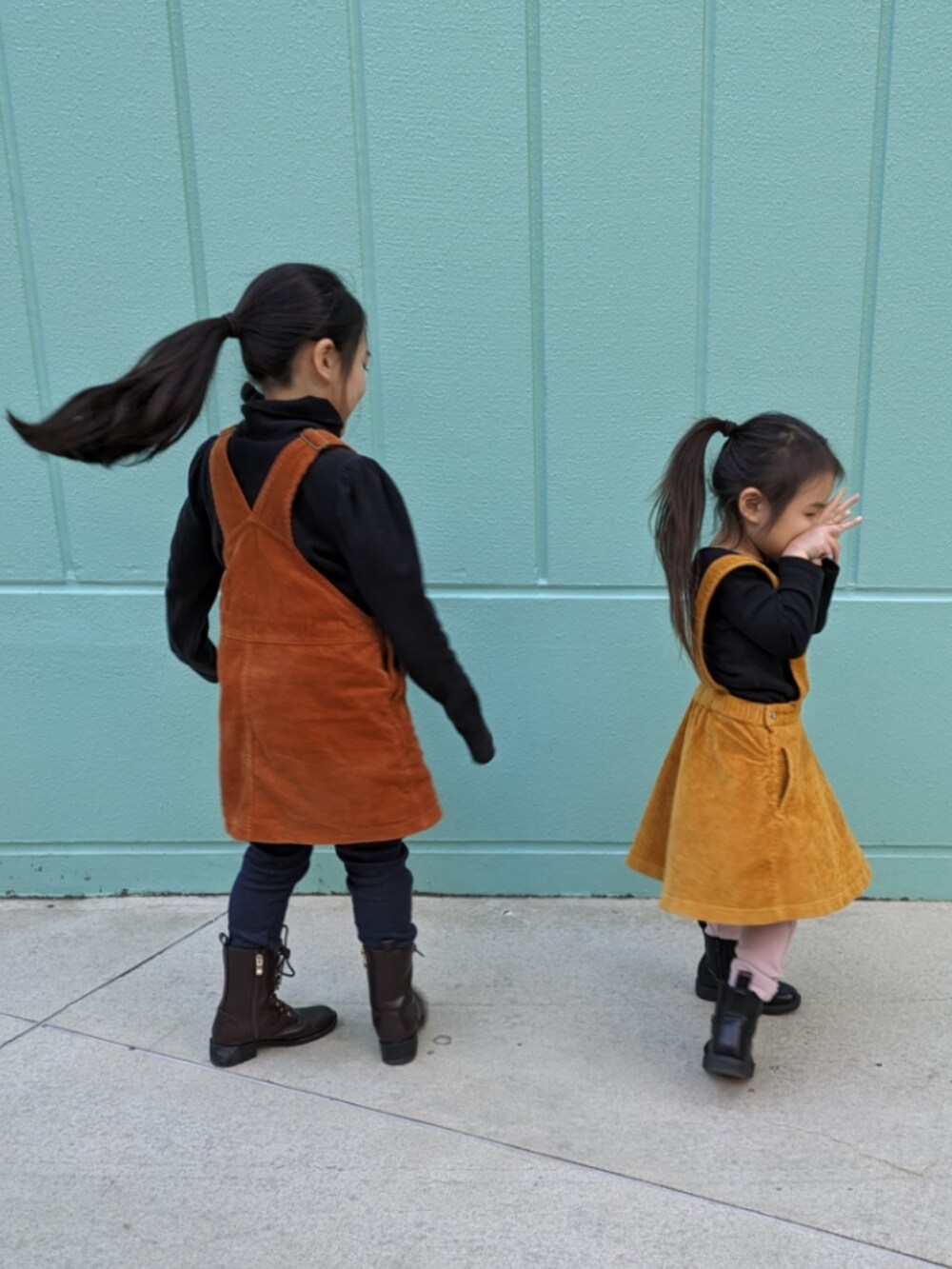 ブラウン系のブーツ、ブラック系のブーツ、オレンジ系のジャンパースカートを着用したキッズの冬コーディネートの2枚目の写真