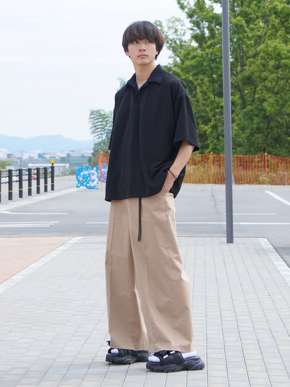 ブラック系のポロシャツ、ベージュ系のチノパンツ、ブラック系のサンダルを着用したメンズの夏コーディネートの2枚目の写真