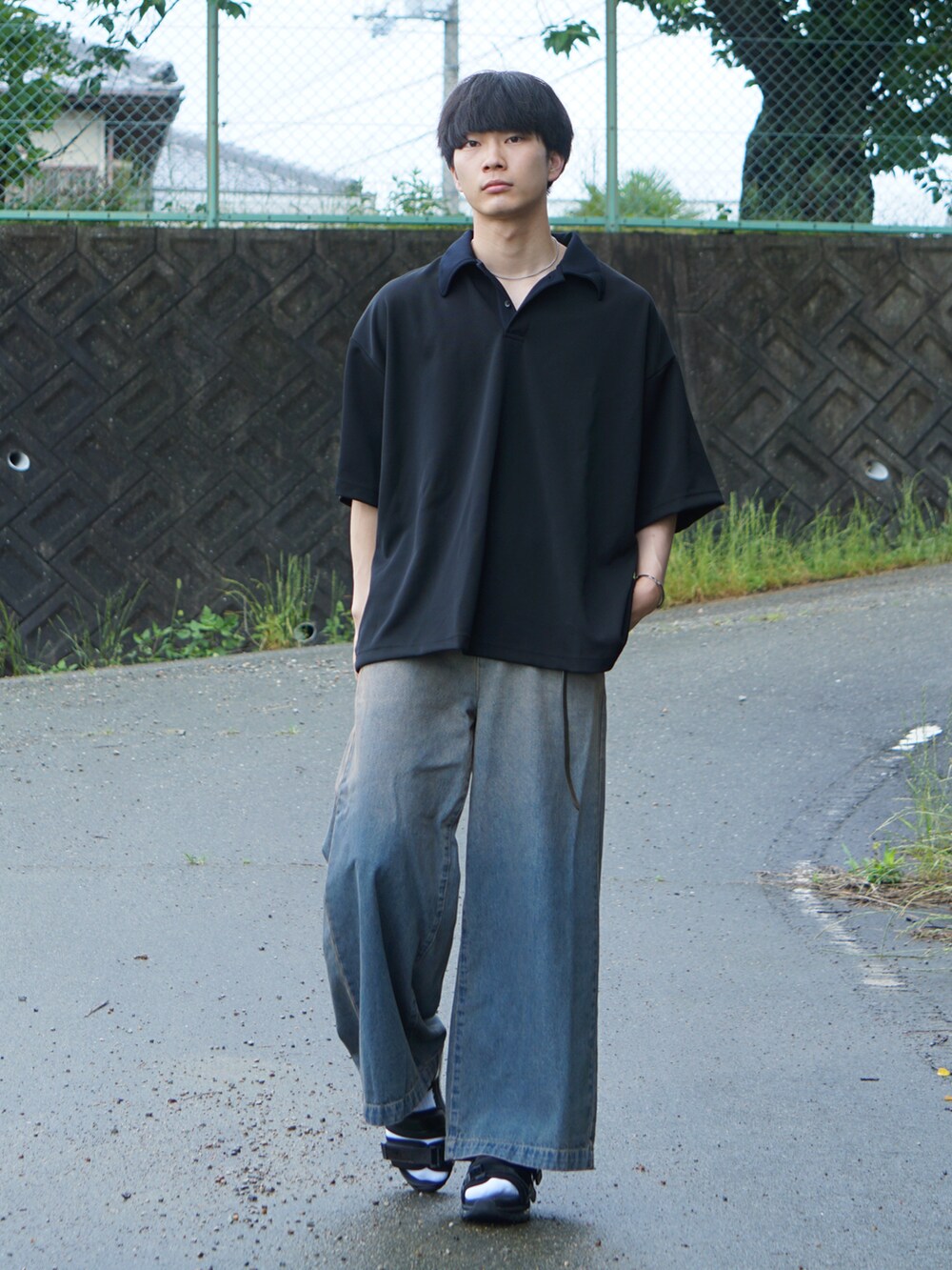 ブラック系のポロシャツ、ブルー系のデニムパンツ、ホワイト系のサンダルを着用したメンズの夏コーディネートの2枚目の写真