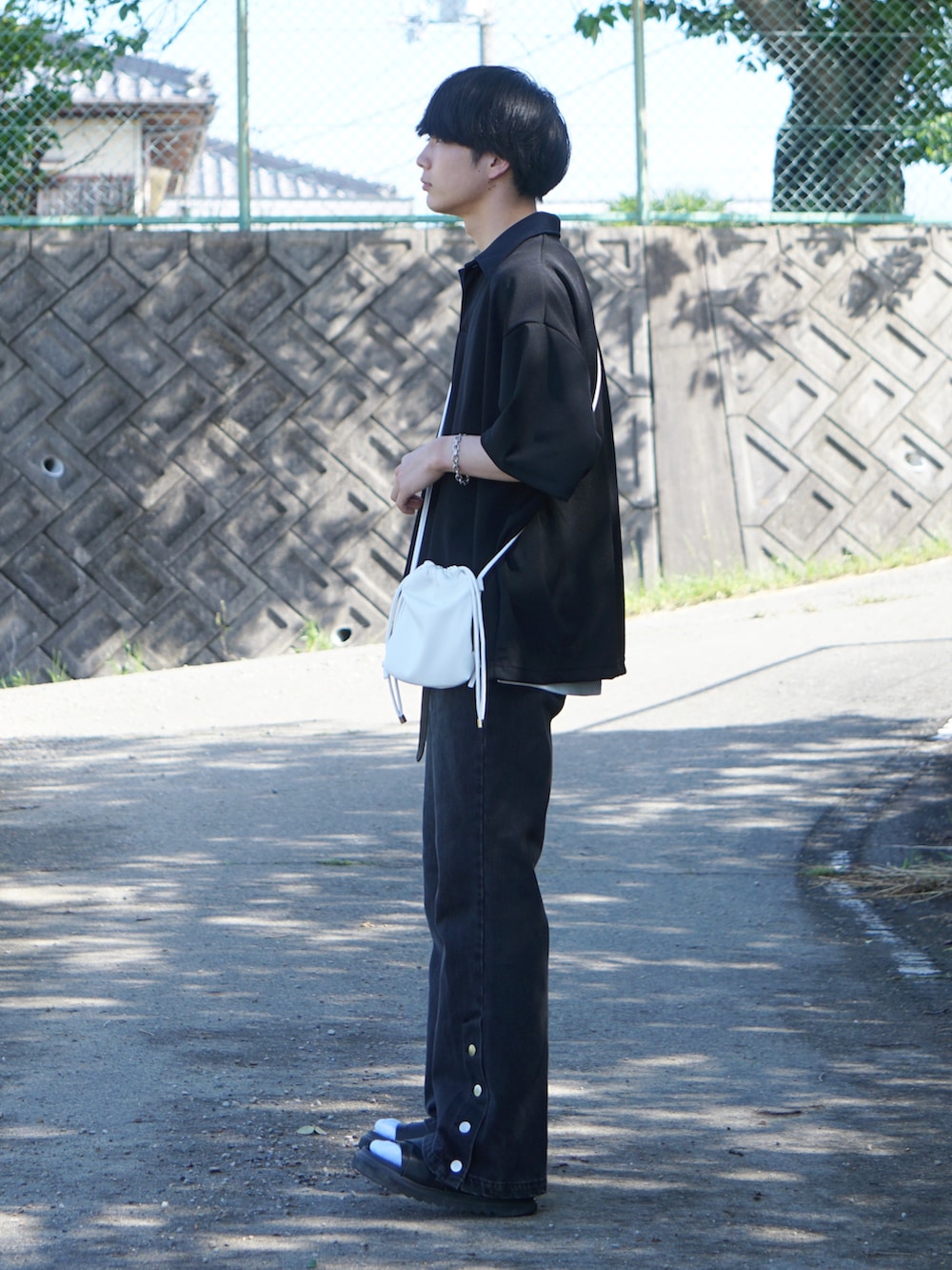 ブラック系のデニムパンツ、ブラック系のサンダル、ブラック系のポロシャツを着用したメンズの夏コーディネートの3枚目の写真