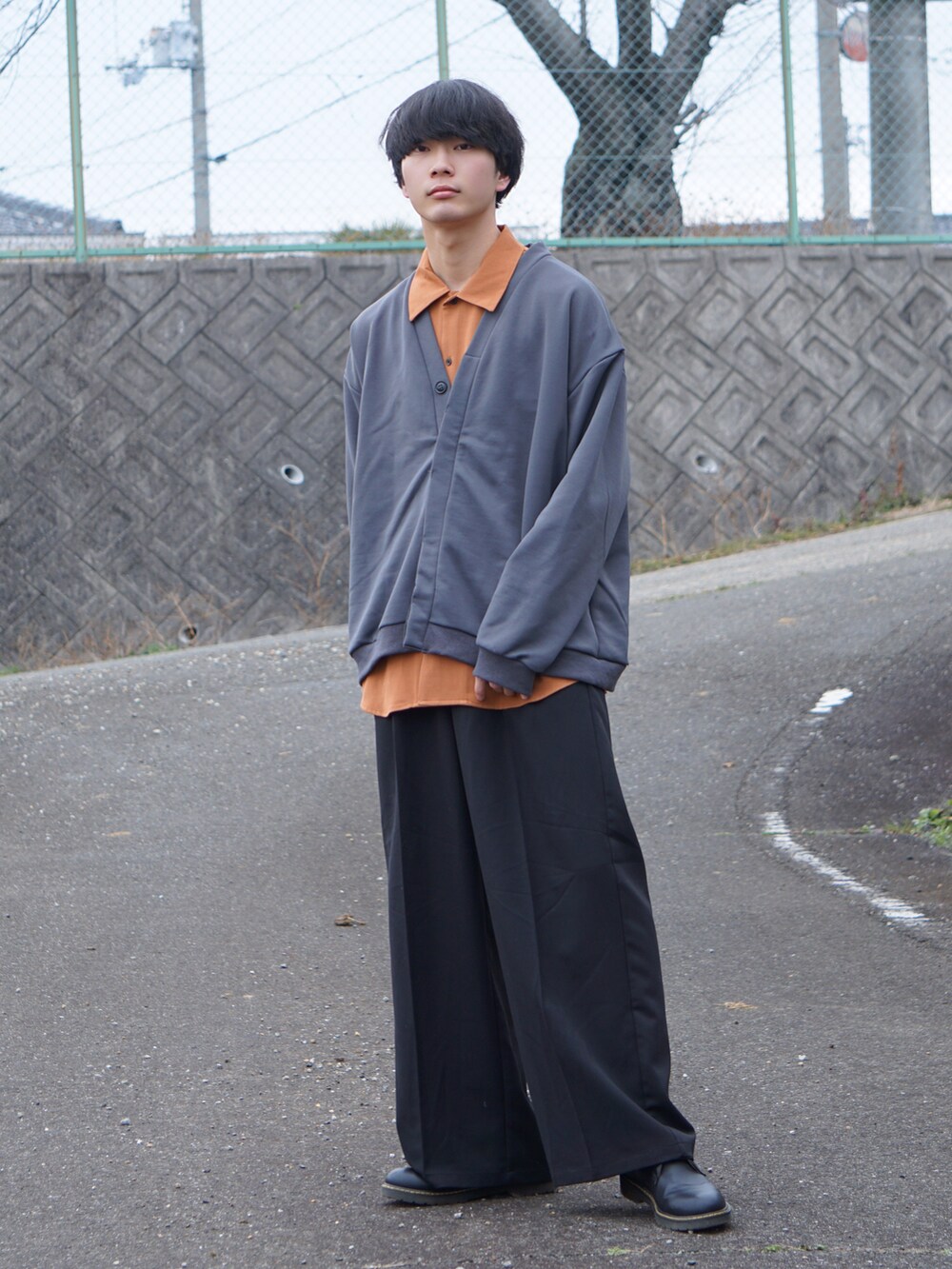 ブラック系のスラックス、グレー系のカーディガン/ボレロ、オレンジ系のシャツ/ブラウスを着用したメンズの冬コーディネートの2枚目の写真