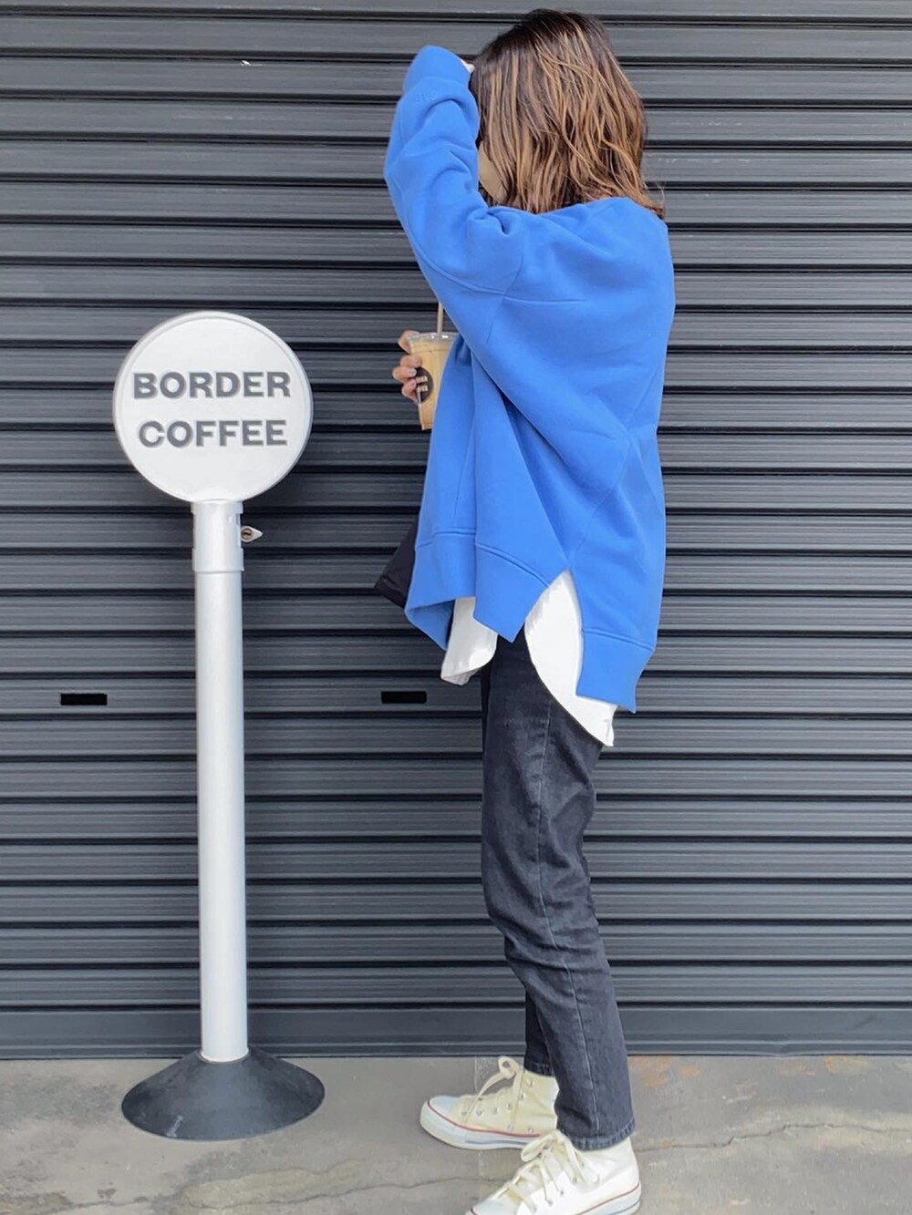 ブルー系のスウェット、ホワイト系のスニーカー、ブラック系のデニムパンツを着用したレディースの春コーディネートの3枚目の写真