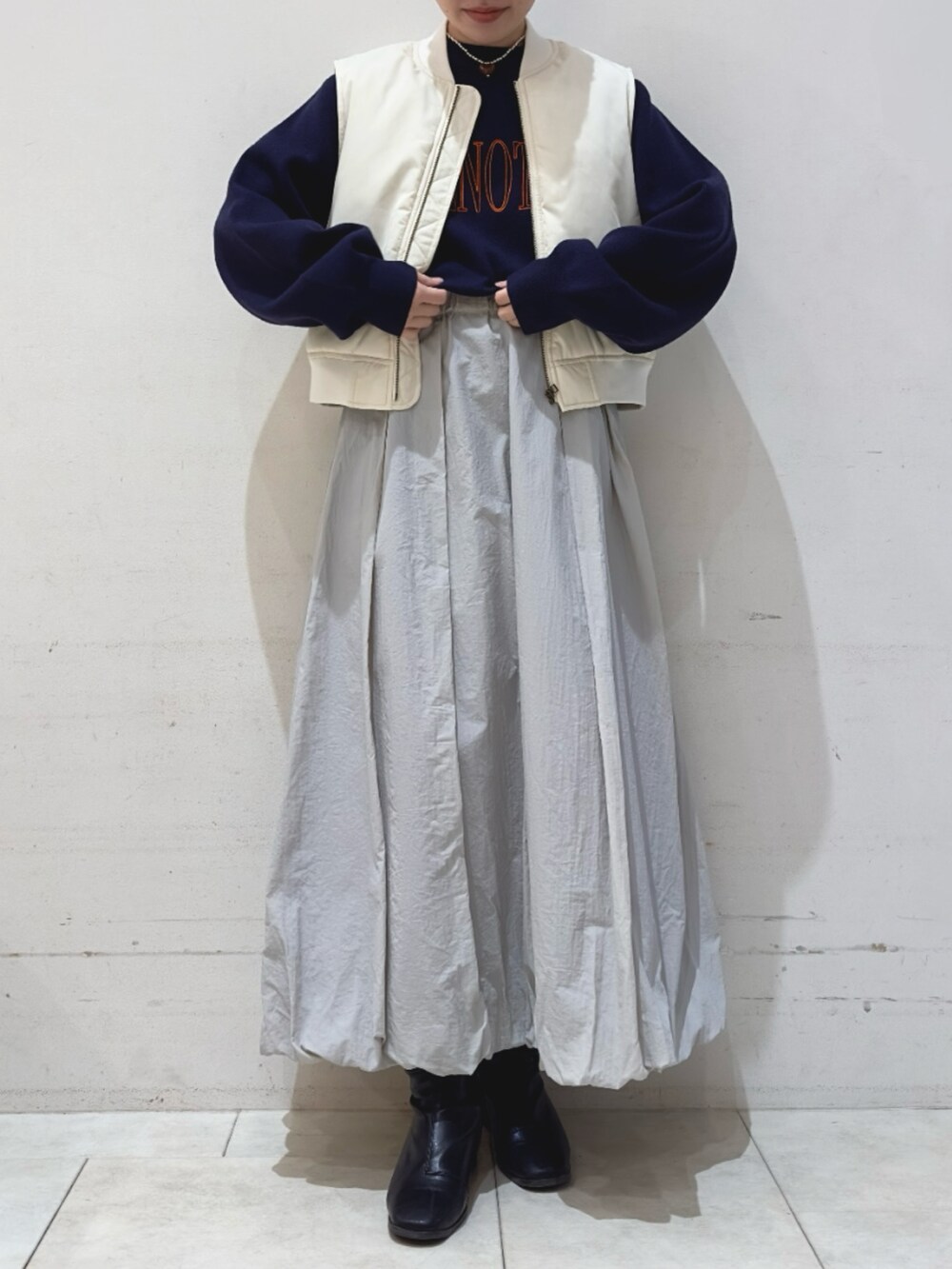 グレー系のスカート、ブルー系のニット/セーター、ホワイト系のベストを着用したレディースの冬コーディネートの2枚目の写真