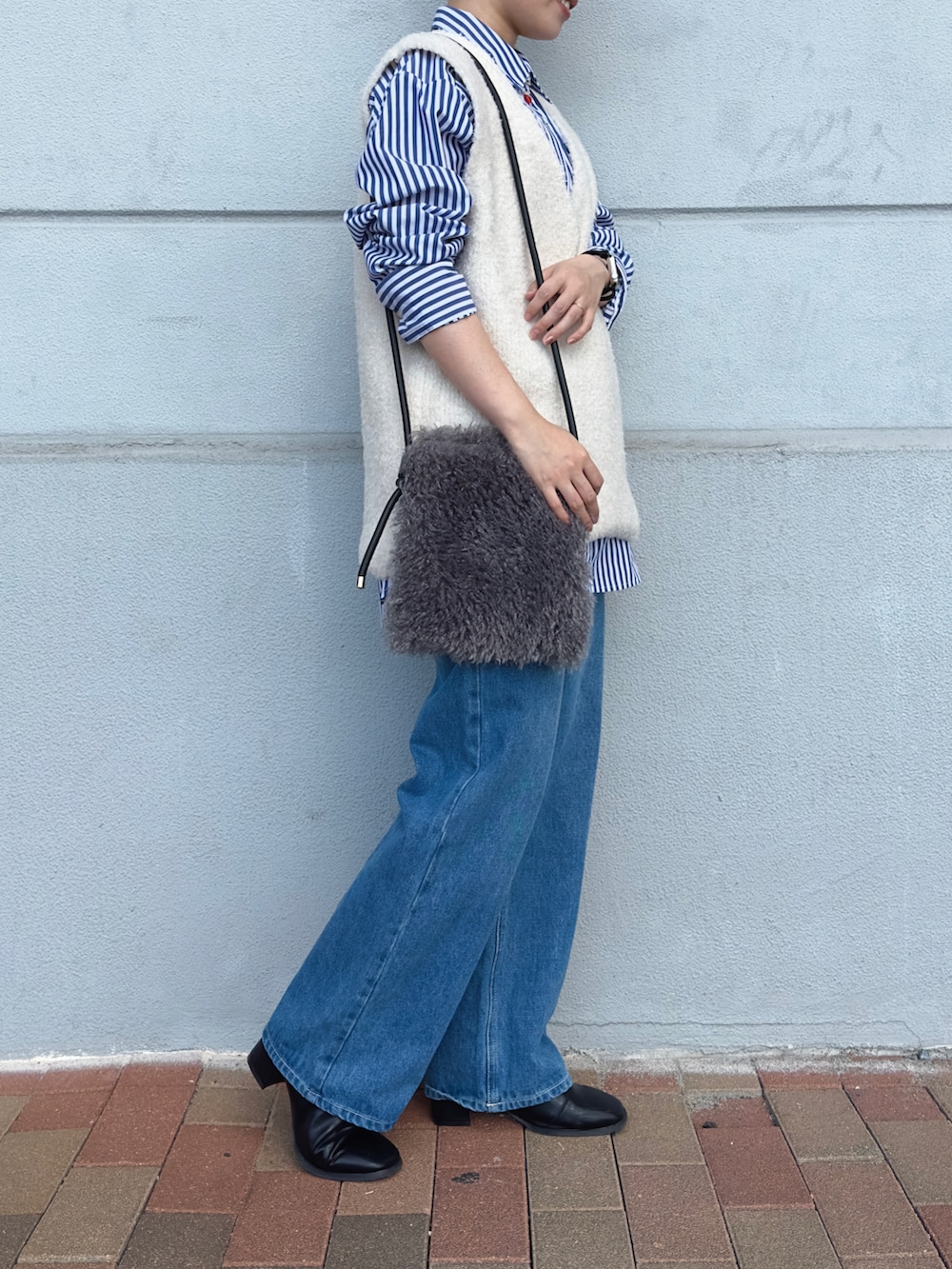 ブルー系のデニムパンツ、ホワイト系のベスト、グレー系のハンドバッグを着用したレディースの秋コーディネートの2枚目の写真