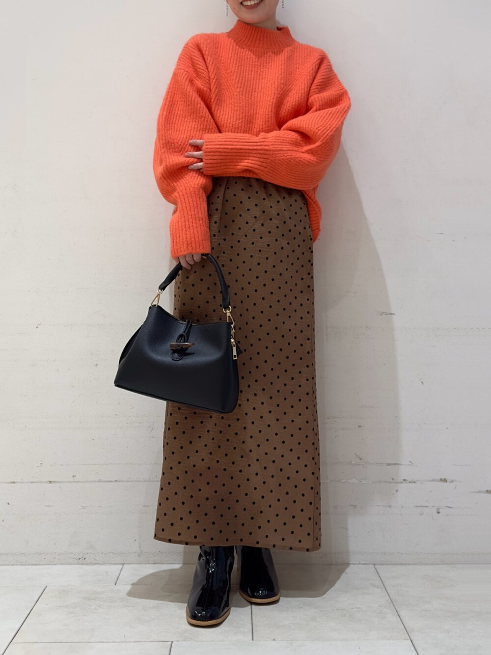オレンジ系のニット/セーター、ベージュ系のスカート、ブラック系のハンドバッグを着用したレディースの冬コーディネートの2枚目の写真