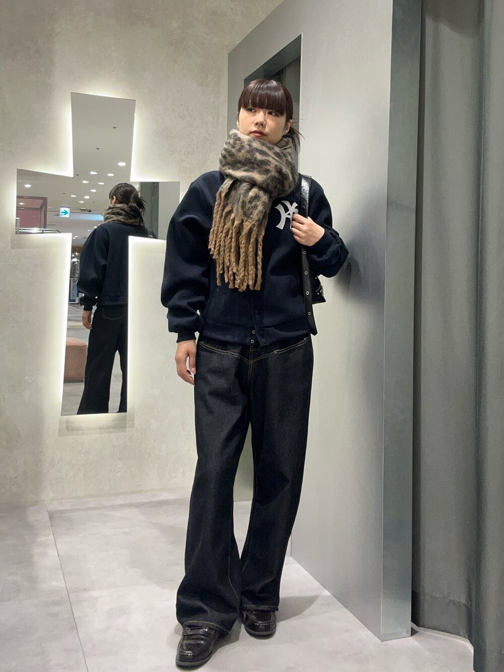 ブルー系のデニムパンツ、ブルー系のスタジャン、ブラウン系のマフラーを着用したレディースの秋コーディネートの2枚目の写真