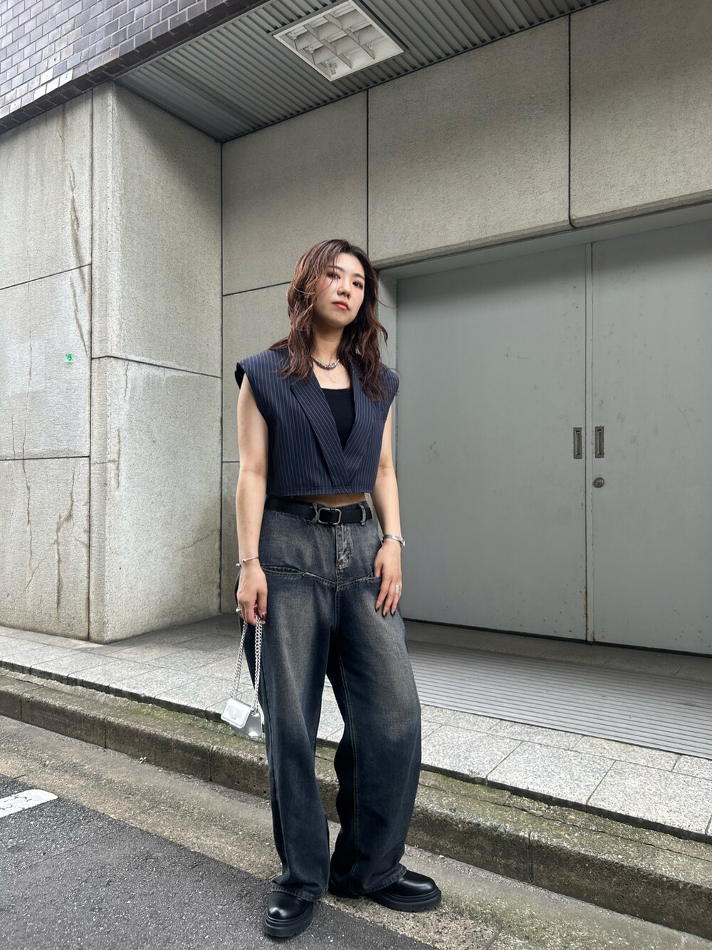 ブルー系のデニムパンツ、グレー系のベスト、ブラック系のショルダーバッグを着用したレディースの秋コーディネートの2枚目の写真