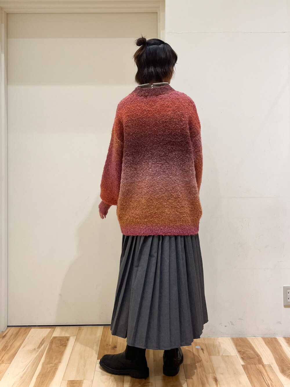 オレンジ系のニット/セーター、グレー系のスカート、ブラック系のブーツを着用したレディースの秋コーディネートの4枚目の写真
