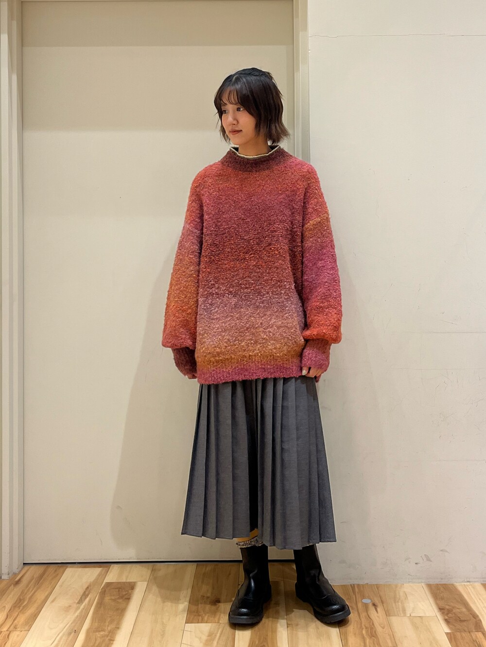 オレンジ系のニット/セーター、グレー系のスカート、ブラック系のブーツを着用したレディースの秋コーディネートの3枚目の写真