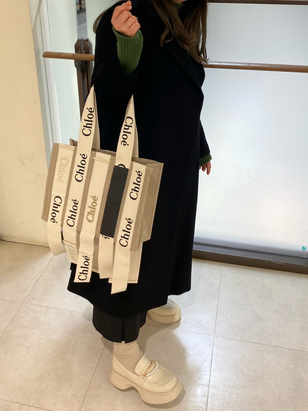 ブラック系のチェスターコート、グリーン系のニット/セーター、ベージュ系のトートバッグを着用したレディースの春コーディネートの2枚目の写真