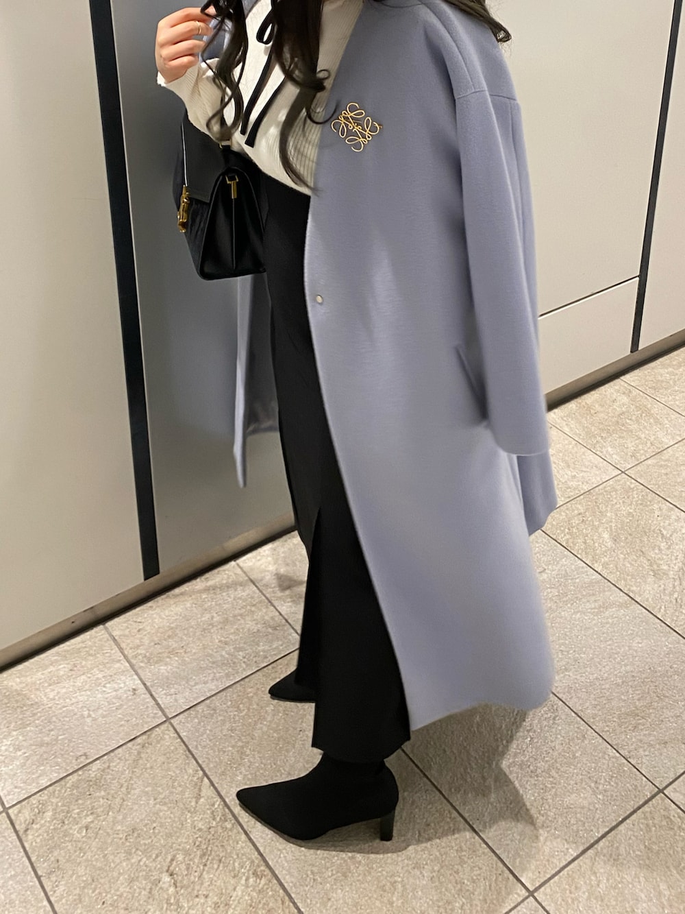 ブラック系のショルダーバッグ、ブルー系のノーカラーコート、ホワイト系のニット/セーターを着用したレディースの冬コーディネートの3枚目の写真