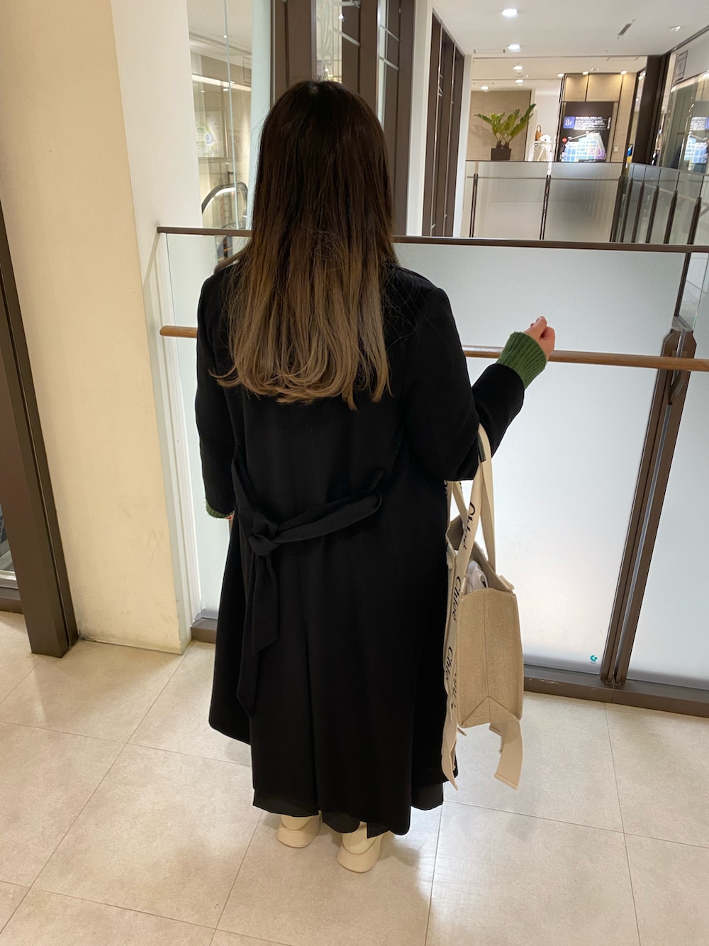 ブラック系のチェスターコート、グリーン系のニット/セーター、ベージュ系のトートバッグを着用したレディースの春コーディネートの4枚目の写真