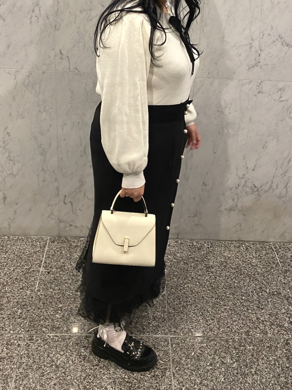ホワイト系のハンドバッグ、ブラック系のローファー、ブラック系のスカートを着用したレディースの冬コーディネートの2枚目の写真