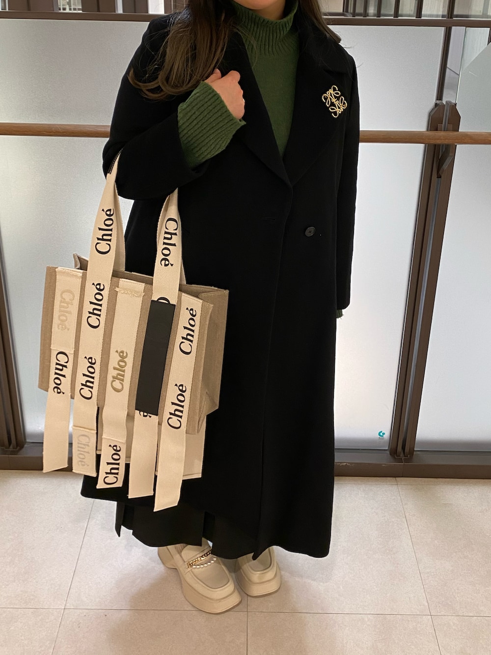 ブラック系のチェスターコート、グリーン系のニット/セーター、ベージュ系のトートバッグを着用したレディースの春コーディネートの3枚目の写真
