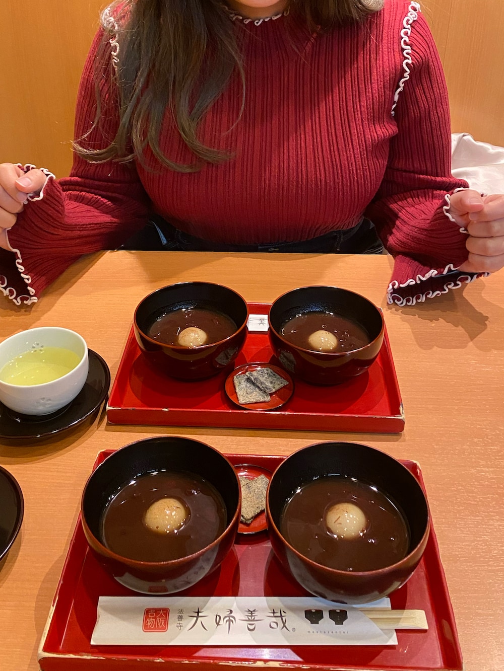 ホワイト系のノーカラーコート、レッド系のニット/セーター、ブルー系のショルダーバッグを着用したレディースの春コーディネートの2枚目の写真