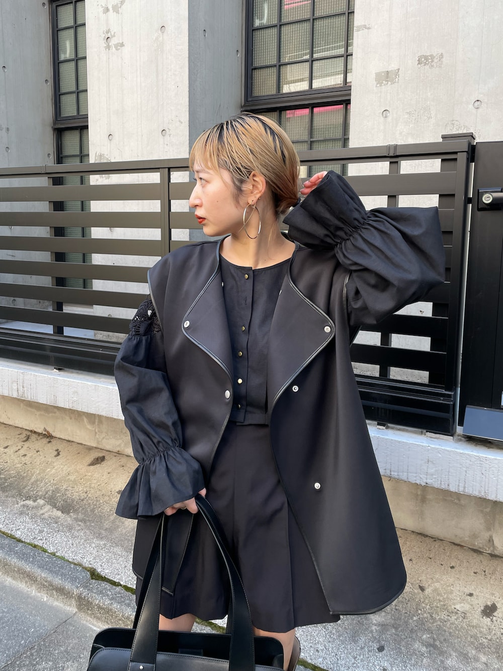 ブラウン系のトートバッグ、ブラック系のベスト、ブラック系のスラックスを着用したレディースの春コーディネートの3枚目の写真