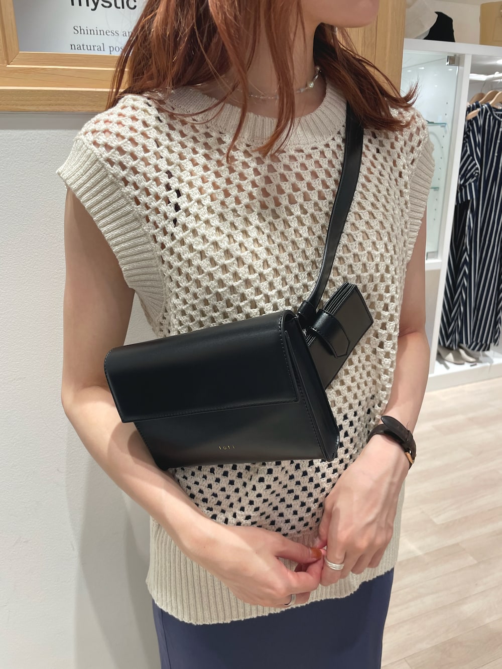 ホワイト系のベスト、ブルー系のスカート、ブラック系のショルダーバッグを着用したレディースの夏コーディネートの2枚目の写真