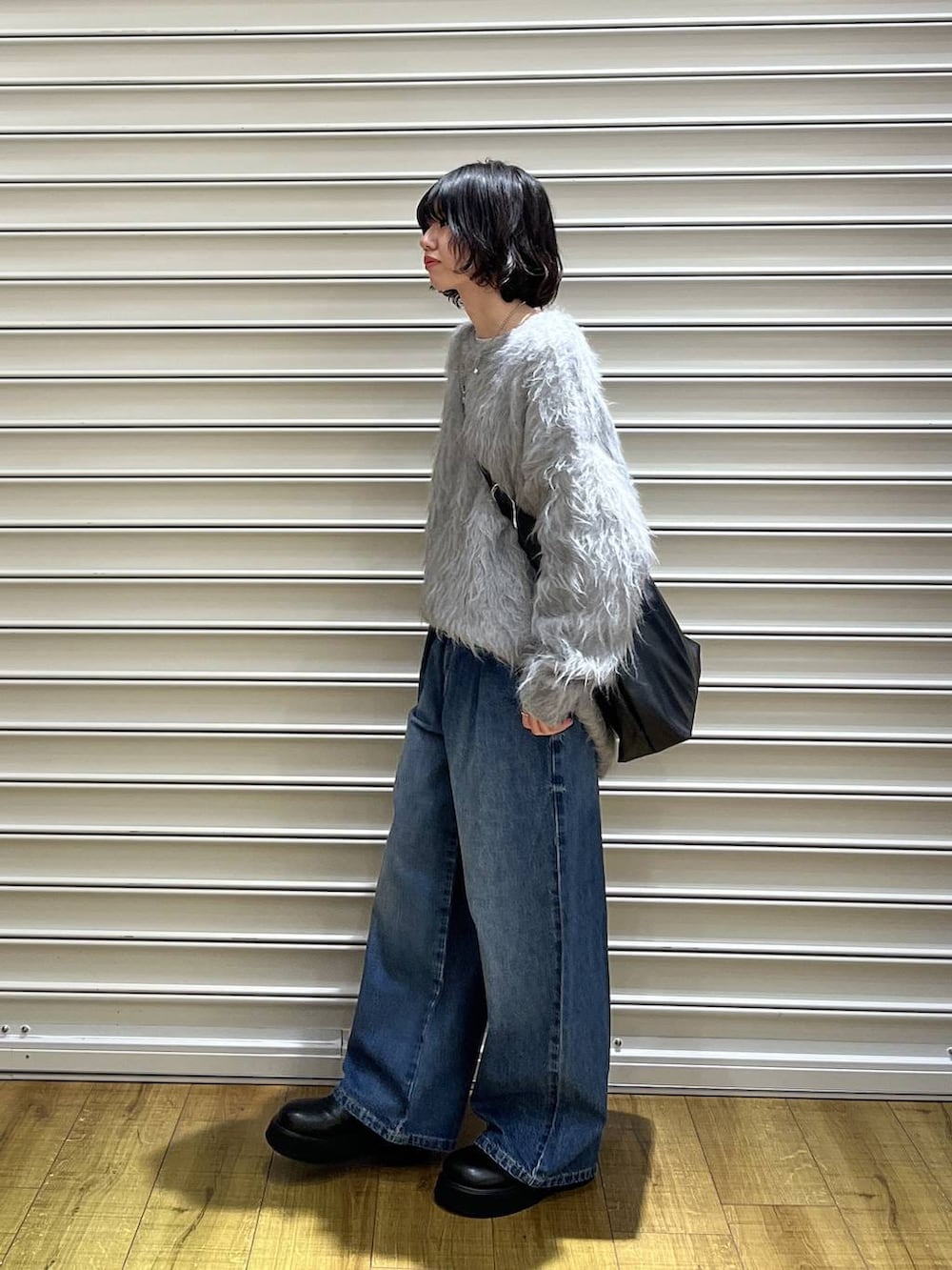 ブラック系のショルダーバッグ、ブラック系のサンダル、ブルー系のデニムパンツを着用したレディースの冬コーディネートの2枚目の写真