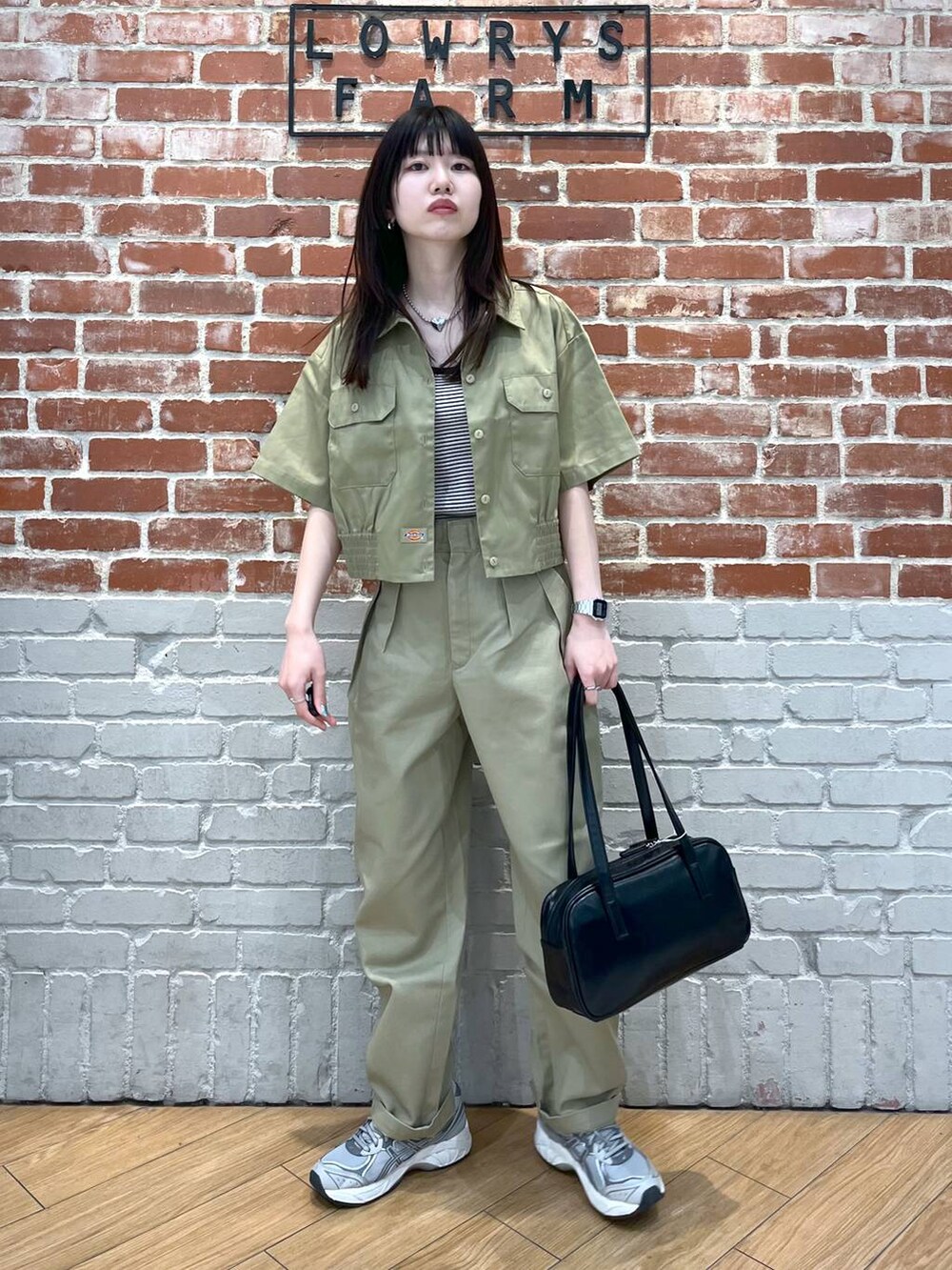 ブラック系のハンドバッグ、ブラック系のタンクトップ、ベージュ系のチノパンツを着用したレディースの春コーディネートの2枚目の写真