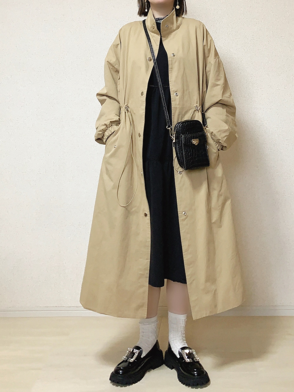 ベージュ系のステンカラーコート、グレー系のTシャツ/カットソー、ブラック系のショルダーバッグを着用したレディースの春コーディネートの2枚目の写真