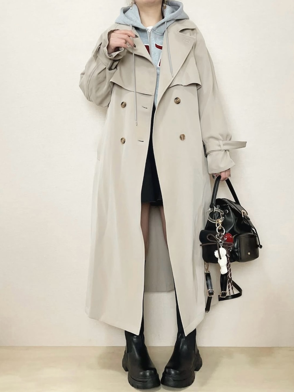 ベージュ系のトレンチコート、グレー系のパーカー、ブラック系のブーツを着用したレディースの冬コーディネートの2枚目の写真