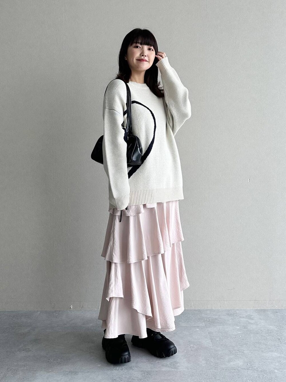 ピンク系のスカート、ブラック系のハンドバッグ、ホワイト系のニット/セーターを着用したレディースの冬コーディネートの2枚目の写真