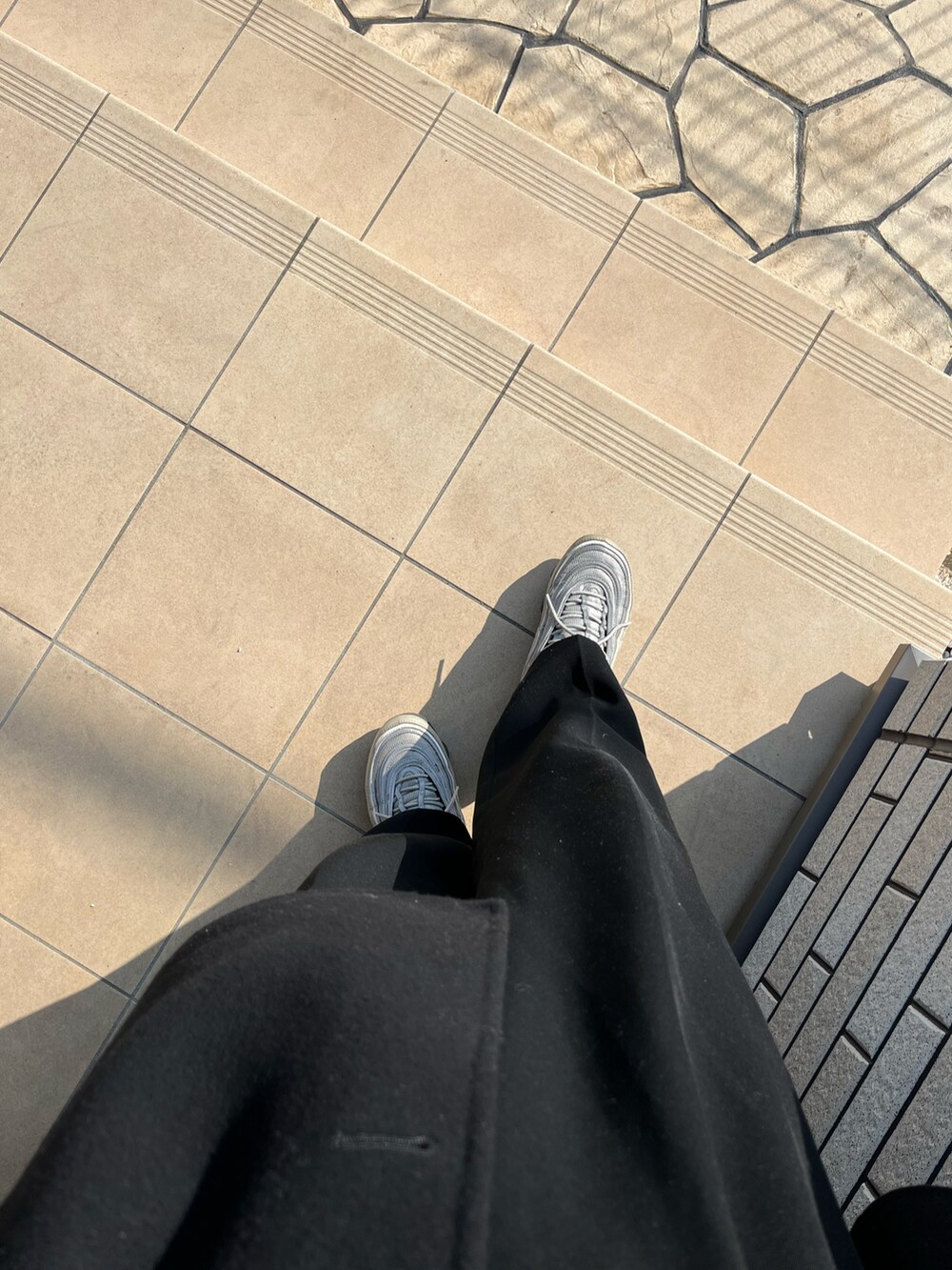 ブラック系のステンカラーコート、ブラック系のボディバッグ/ウエストポーチ、シルバー系のスニーカーを着用したメンズの冬コーディネートの5枚目の写真