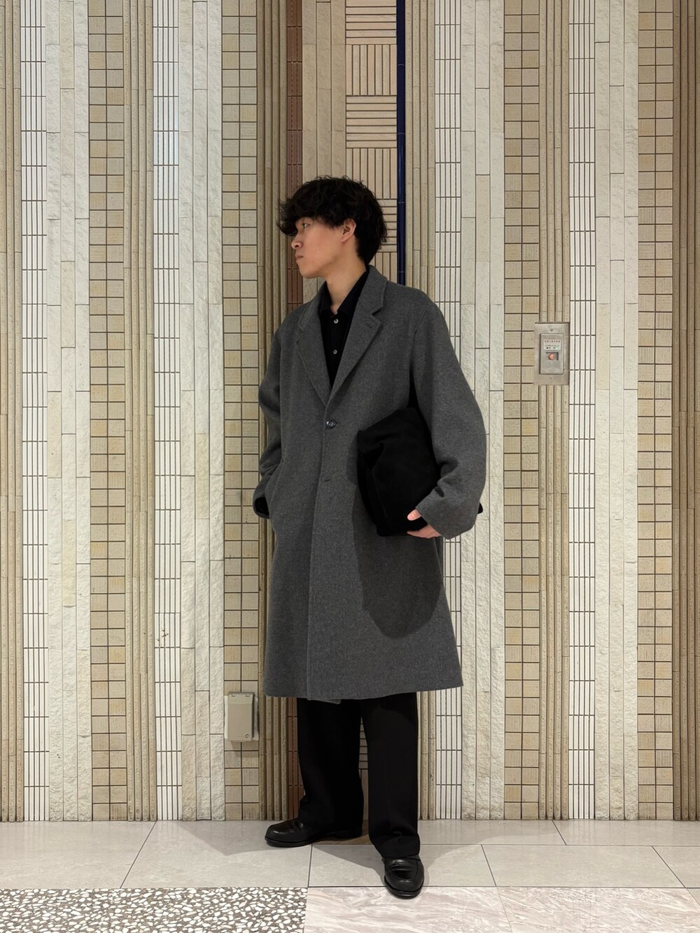 ホワイト系のチェスターコート、グリーン系のトートバッグ、ブラック系のその他パンツを着用したメンズの冬コーディネートの2枚目の写真