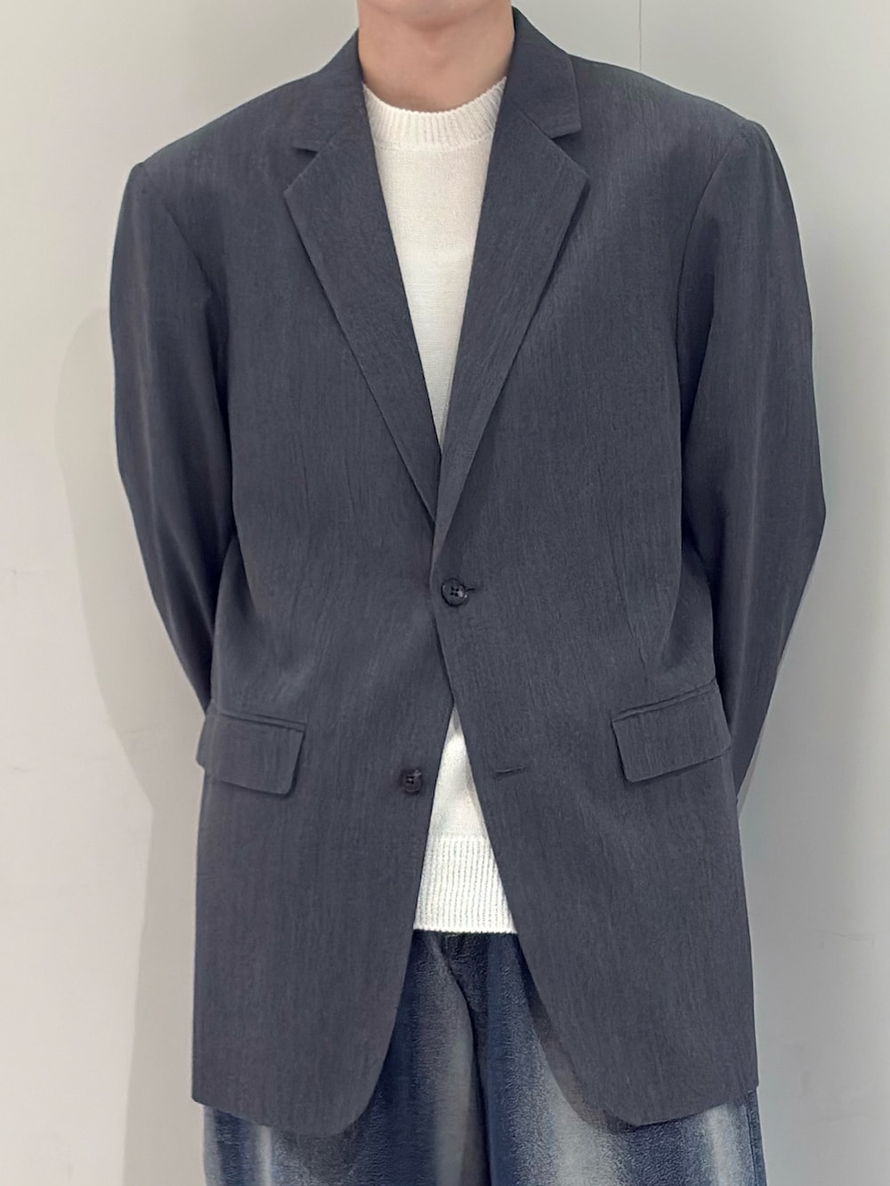 グレー系のテーラードジャケット、ホワイト系のニット/セーター、ブルー系のデニムパンツを着用したメンズの春コーディネートの3枚目の写真