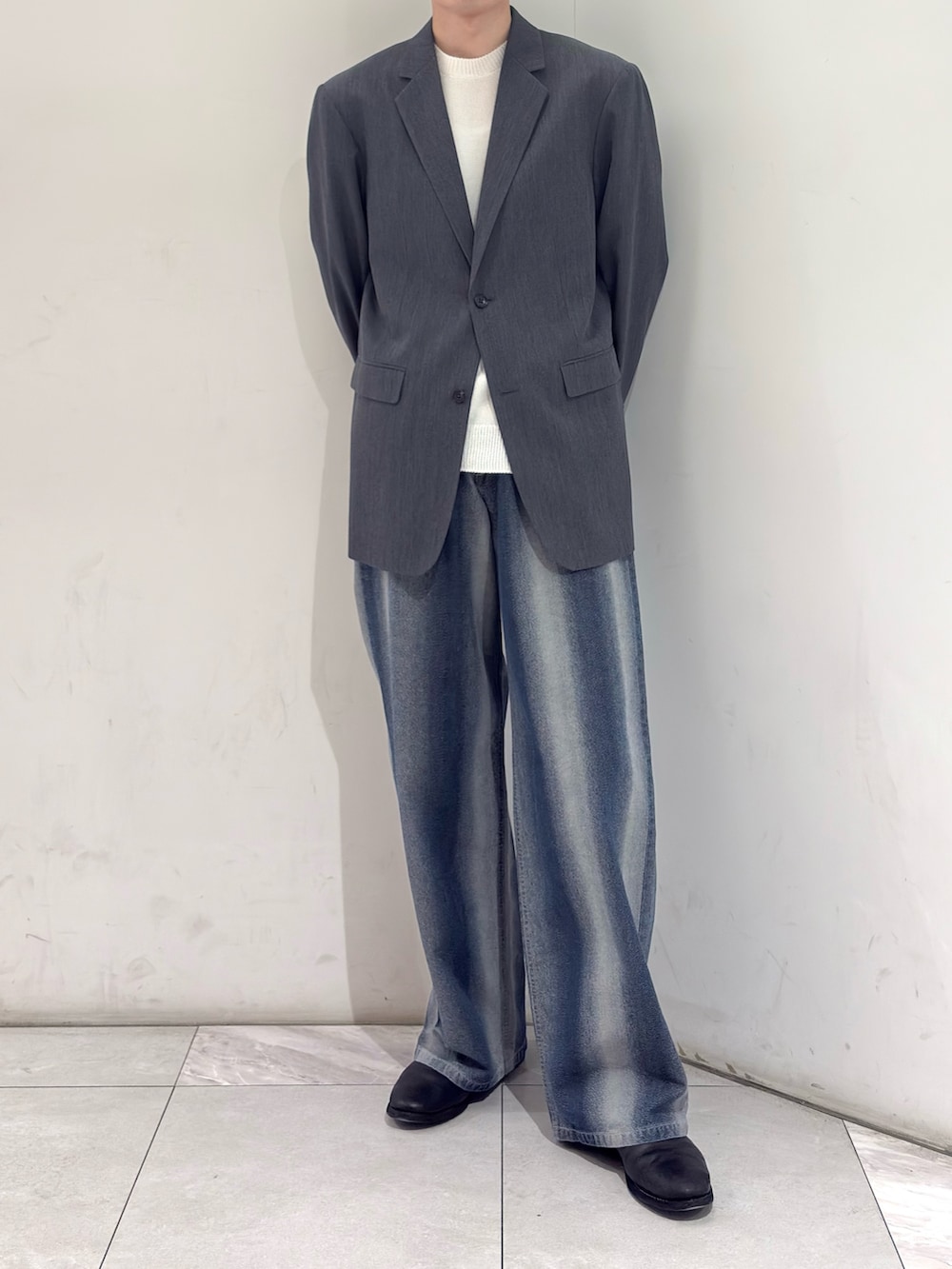 グレー系のテーラードジャケット、ホワイト系のニット/セーター、ブルー系のデニムパンツを着用したメンズの春コーディネートの2枚目の写真