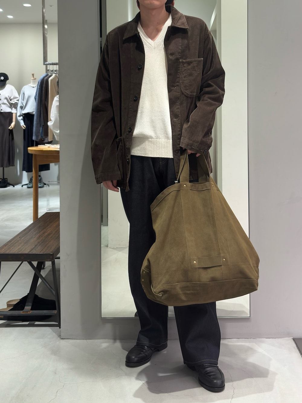 ベージュ系のニット/セーター、グリーン系のトートバッグ、ブルー系のデニムパンツを着用したメンズの秋コーディネートの2枚目の写真
