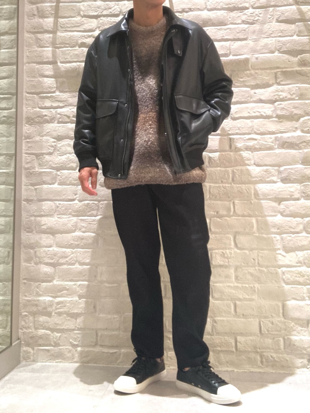 ブラック系のライダースジャケット、ブラウン系のニット/セーター、ブラック系のスラックスを着用したメンズの秋コーディネートの2枚目の写真