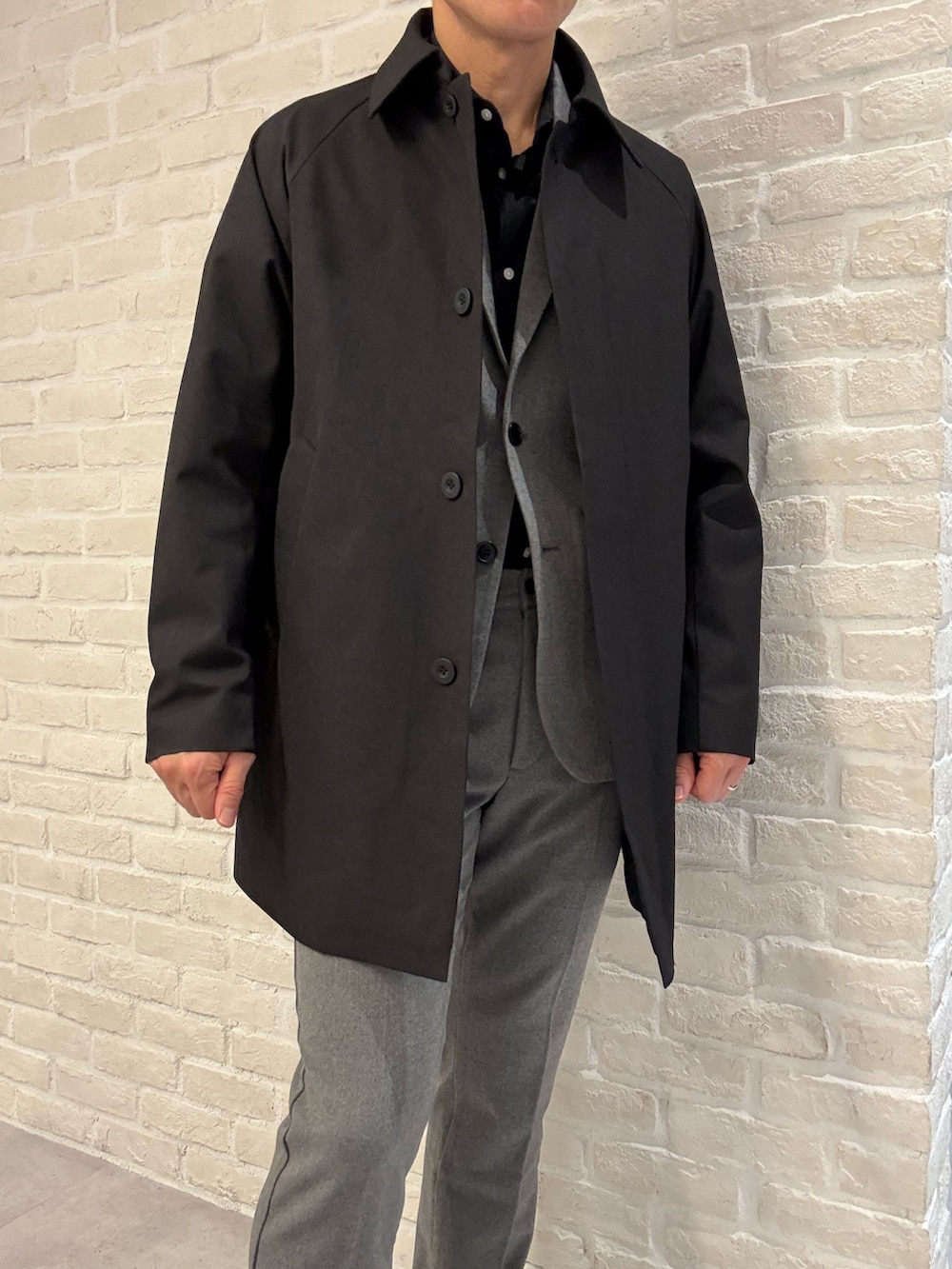 ブラック系のステンカラーコート、グレー系のセットアップ、グレー系のテーラードジャケットを着用したメンズの冬コーディネートの3枚目の写真