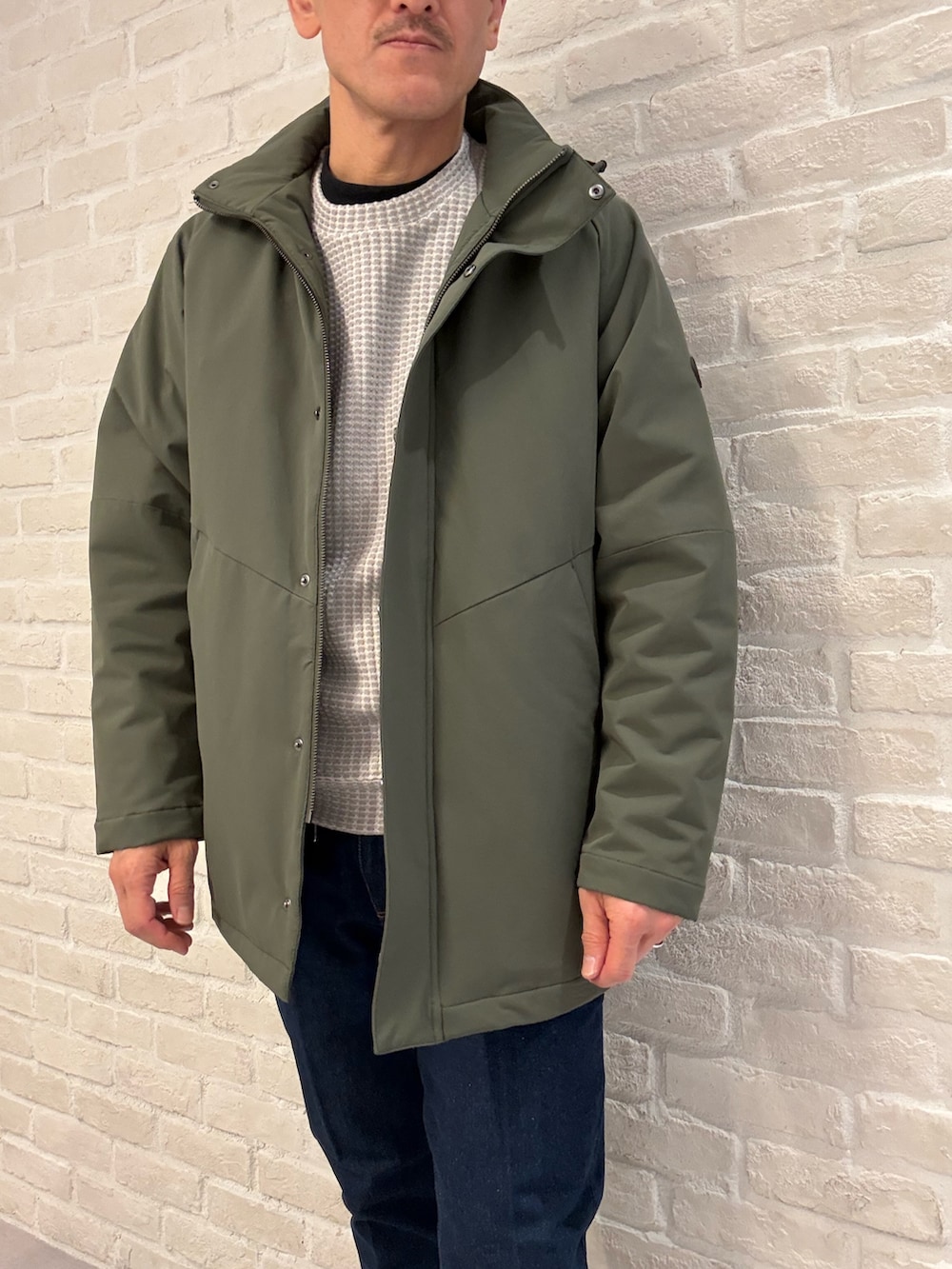 グリーン系のブルゾン、ベージュ系のTシャツ/カットソー、ブルー系のデニムパンツを着用したメンズの冬コーディネートの4枚目の写真