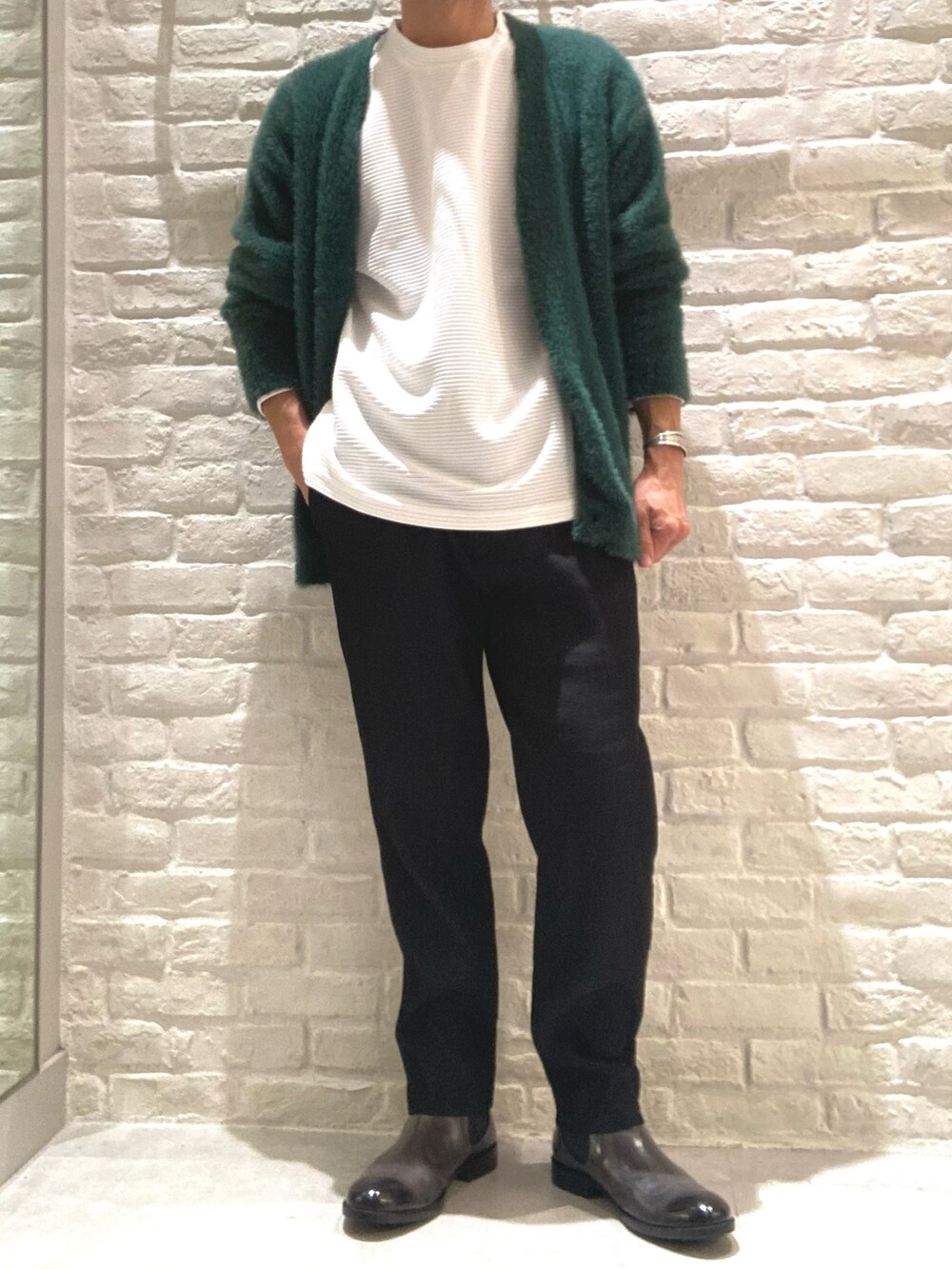 グリーン系のカーディガン/ボレロ、ホワイト系のTシャツ/カットソー、ブラック系のスラックスを着用したメンズの秋コーディネートの2枚目の写真