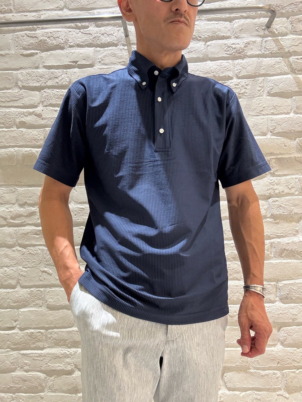 ブルー系のポロシャツ、グレー系のスラックス、ブラック系のトートバッグを着用したメンズの夏コーディネートの2枚目の写真