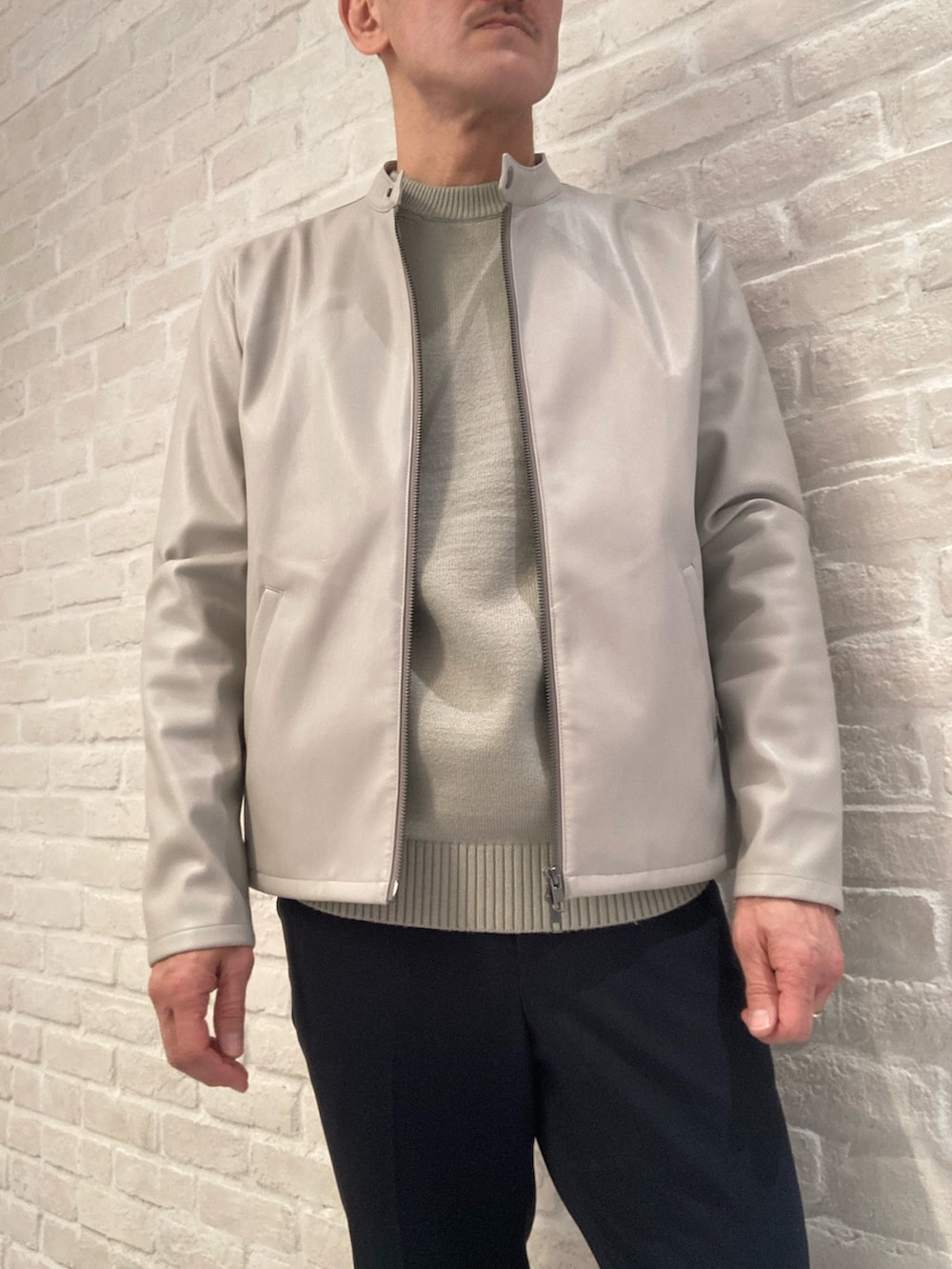 グレー系のライダースジャケット、グリーン系のニット/セーター、ブルー系のスラックスを着用したメンズの春コーディネートの2枚目の写真