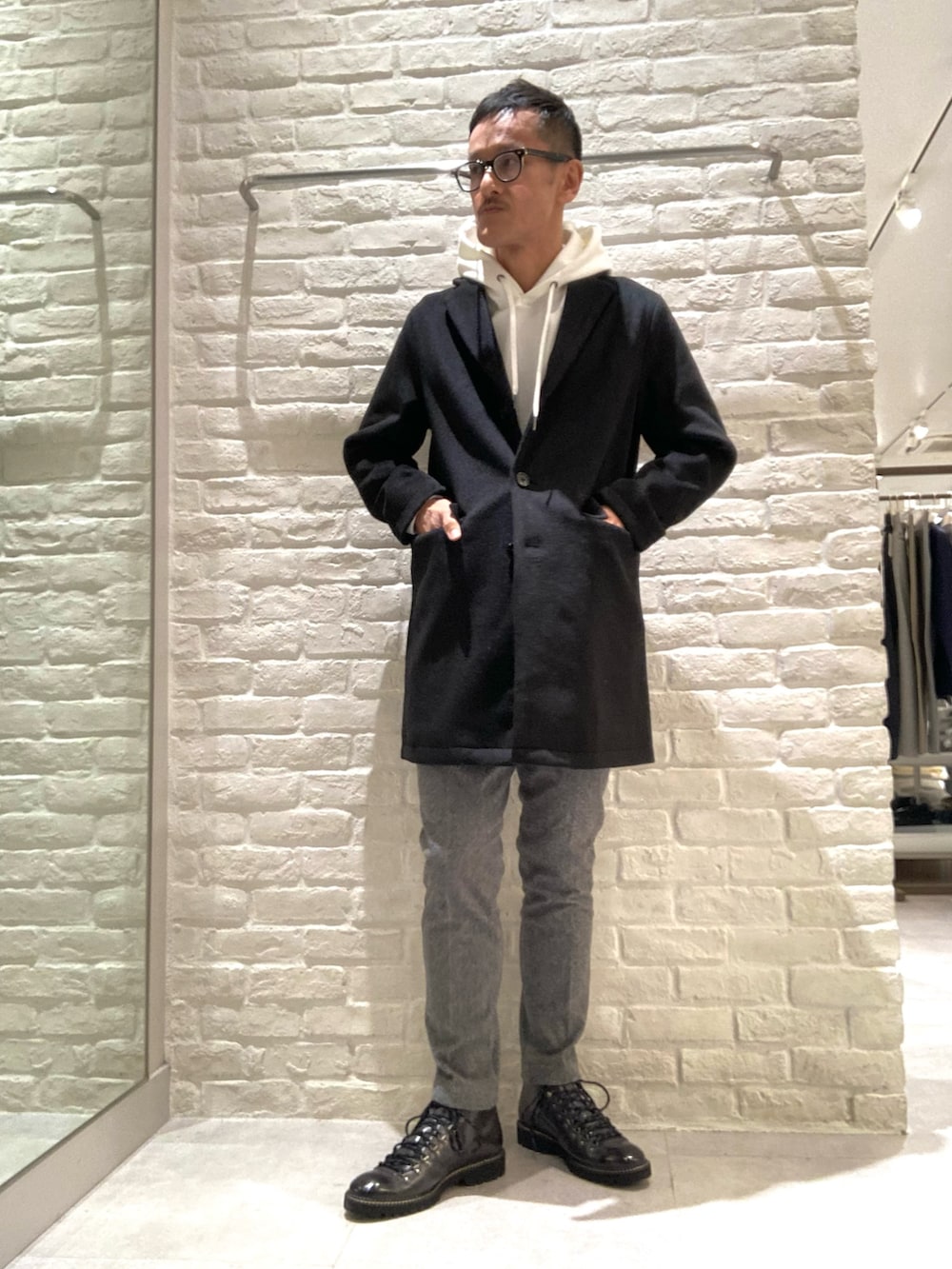 ブラック系のチェスターコート、ホワイト系のパーカー、グレー系のスラックスを着用したメンズの秋コーディネートの3枚目の写真