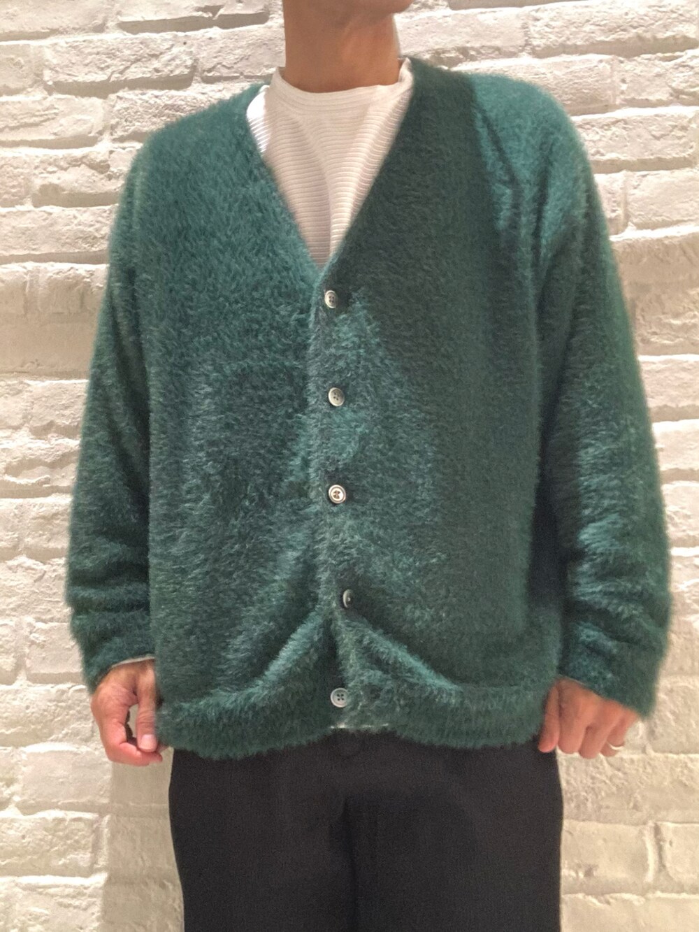 グリーン系のカーディガン/ボレロ、ホワイト系のTシャツ/カットソー、ブラック系のスラックスを着用したメンズの秋コーディネートの4枚目の写真