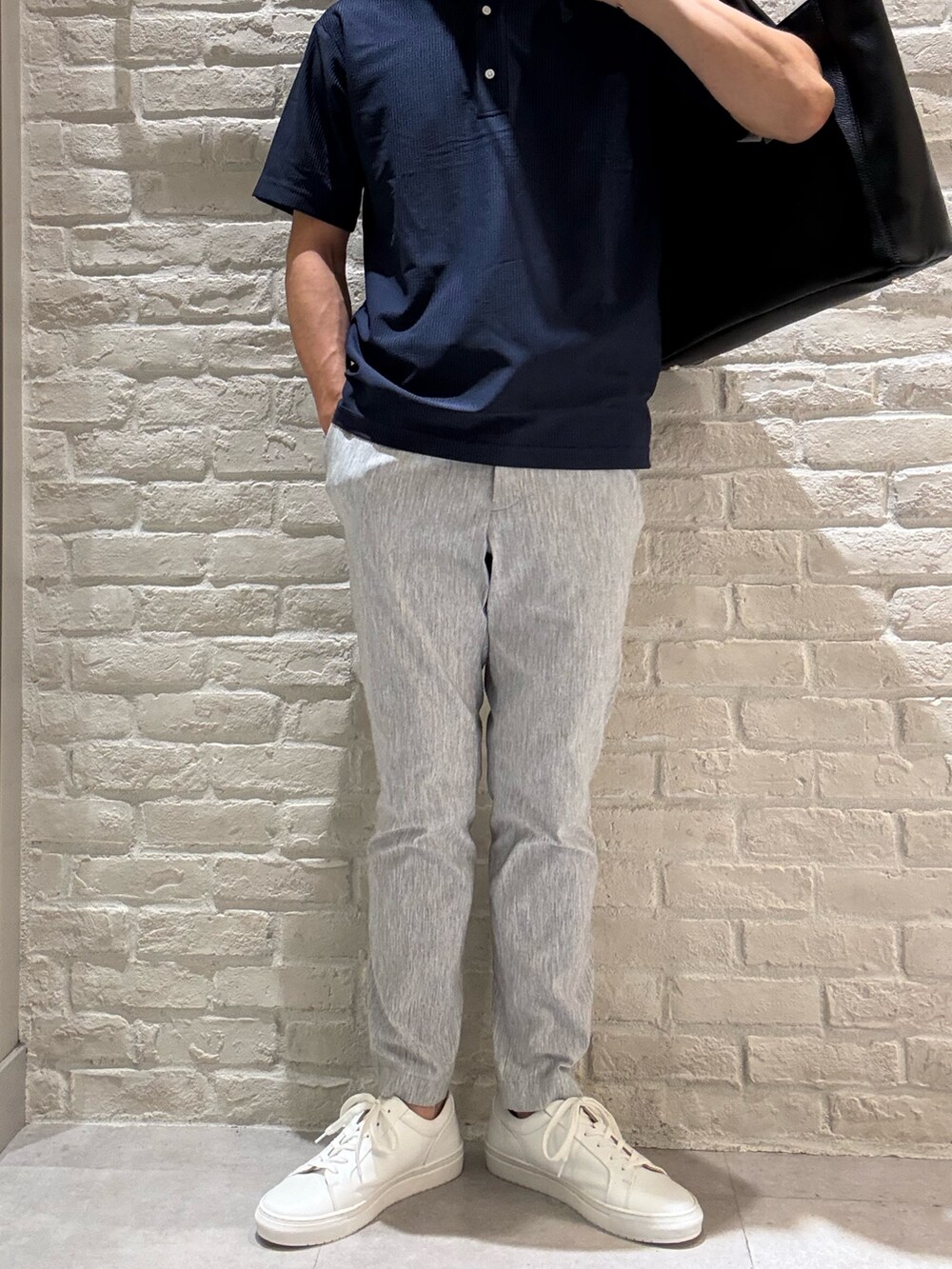 ブルー系のポロシャツ、グレー系のスラックス、ブラック系のトートバッグを着用したメンズの夏コーディネートの4枚目の写真