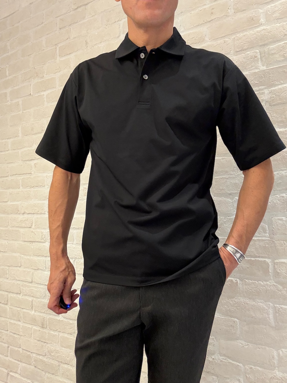 ブラック系のポロシャツ、ブラック系のスラックス、ブラック系のビジネスバッグを着用したメンズの夏コーディネートの2枚目の写真