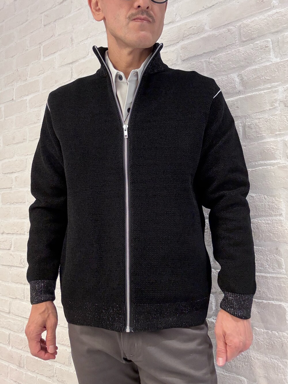 グレー系のチノパンツ、ブラック系のニット/セーター、ベージュ系のシャツ/ブラウスを着用したメンズの秋コーディネートの3枚目の写真