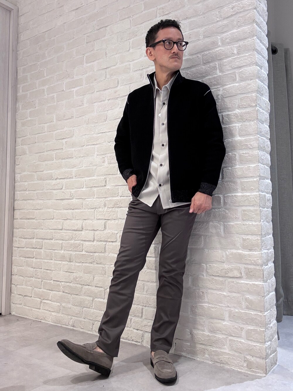 グレー系のチノパンツ、ブラック系のニット/セーター、ベージュ系のシャツ/ブラウスを着用したメンズの秋コーディネートの2枚目の写真
