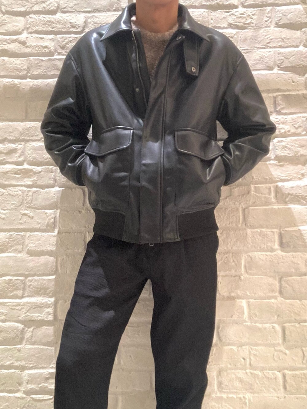 ブラック系のライダースジャケット、ブラウン系のニット/セーター、ブラック系のスラックスを着用したメンズの秋コーディネートの4枚目の写真